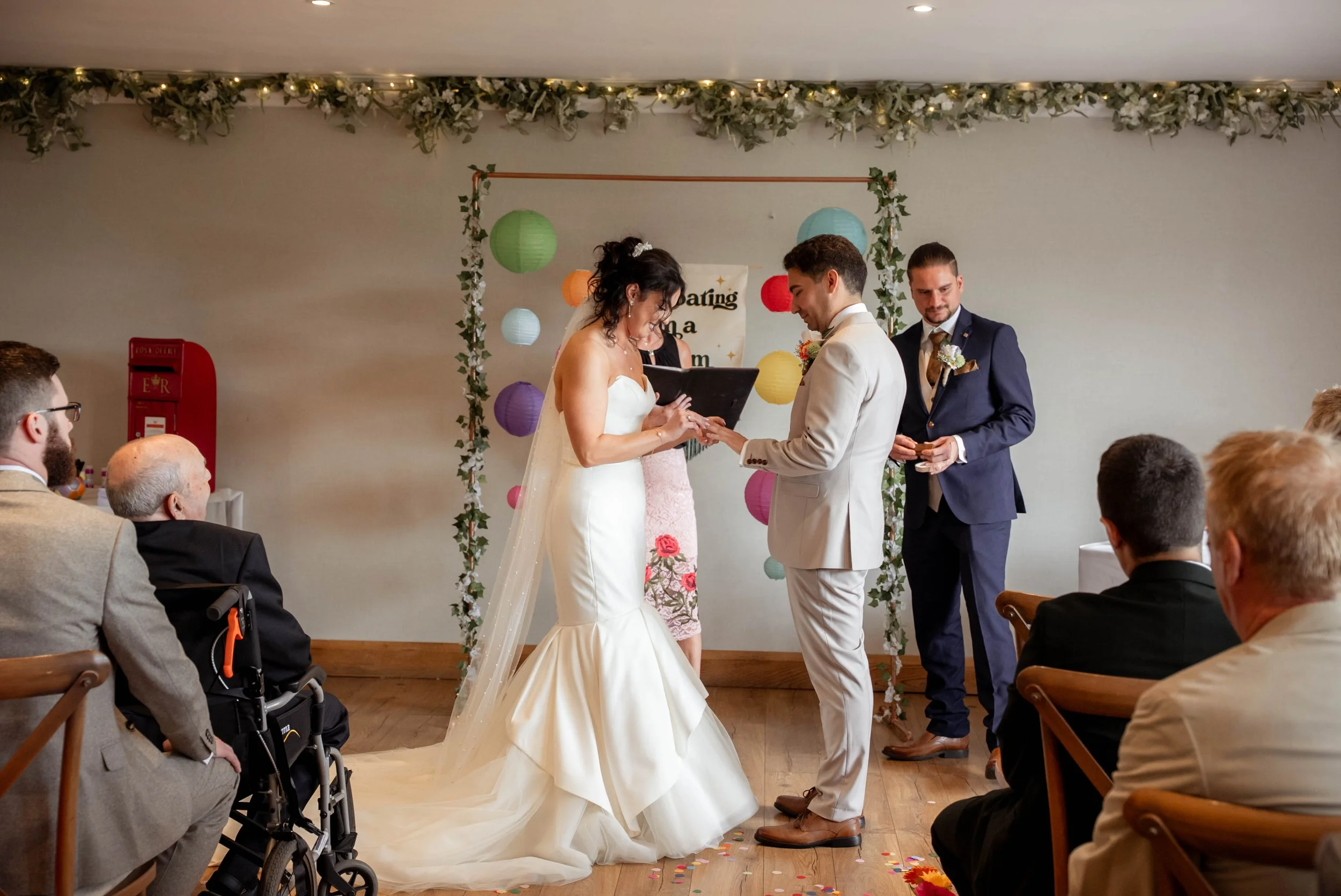 Bride and groom exchanging vows during a wedding ceremony in a decorated indoor venue with guests watching.