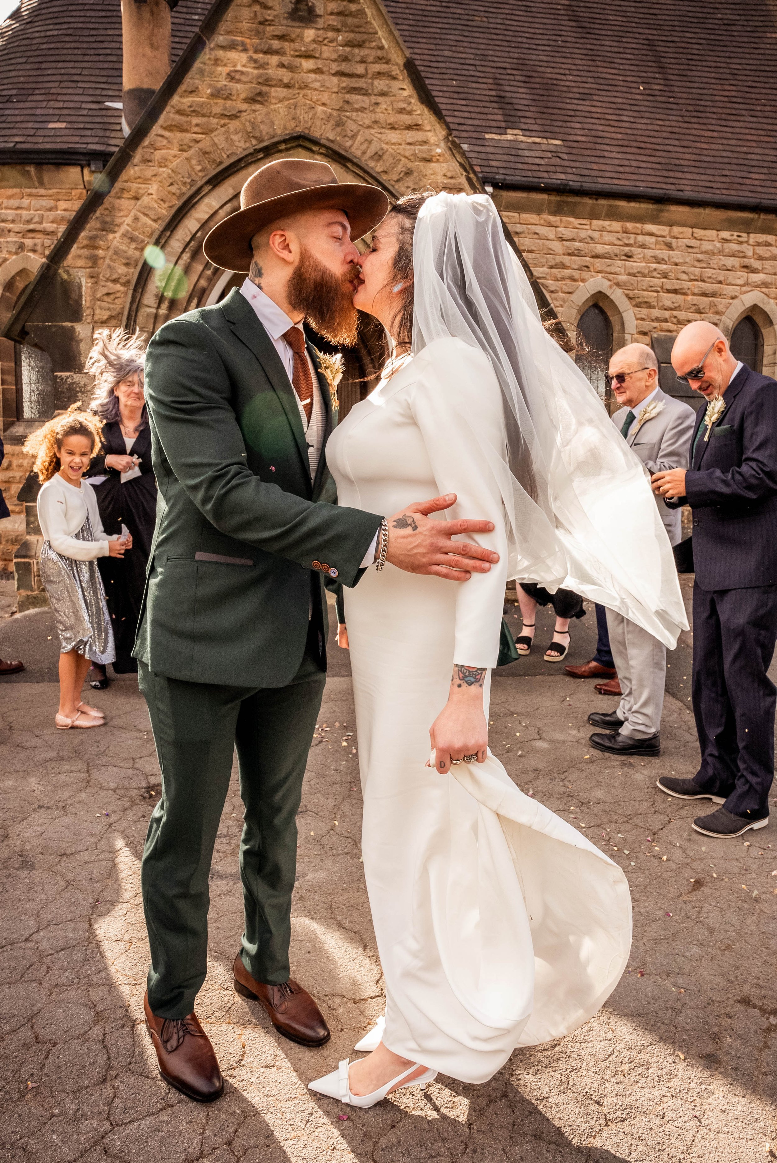 A newlywed couple sharing a kiss outside a church, with friends and family in the background.Nottingham