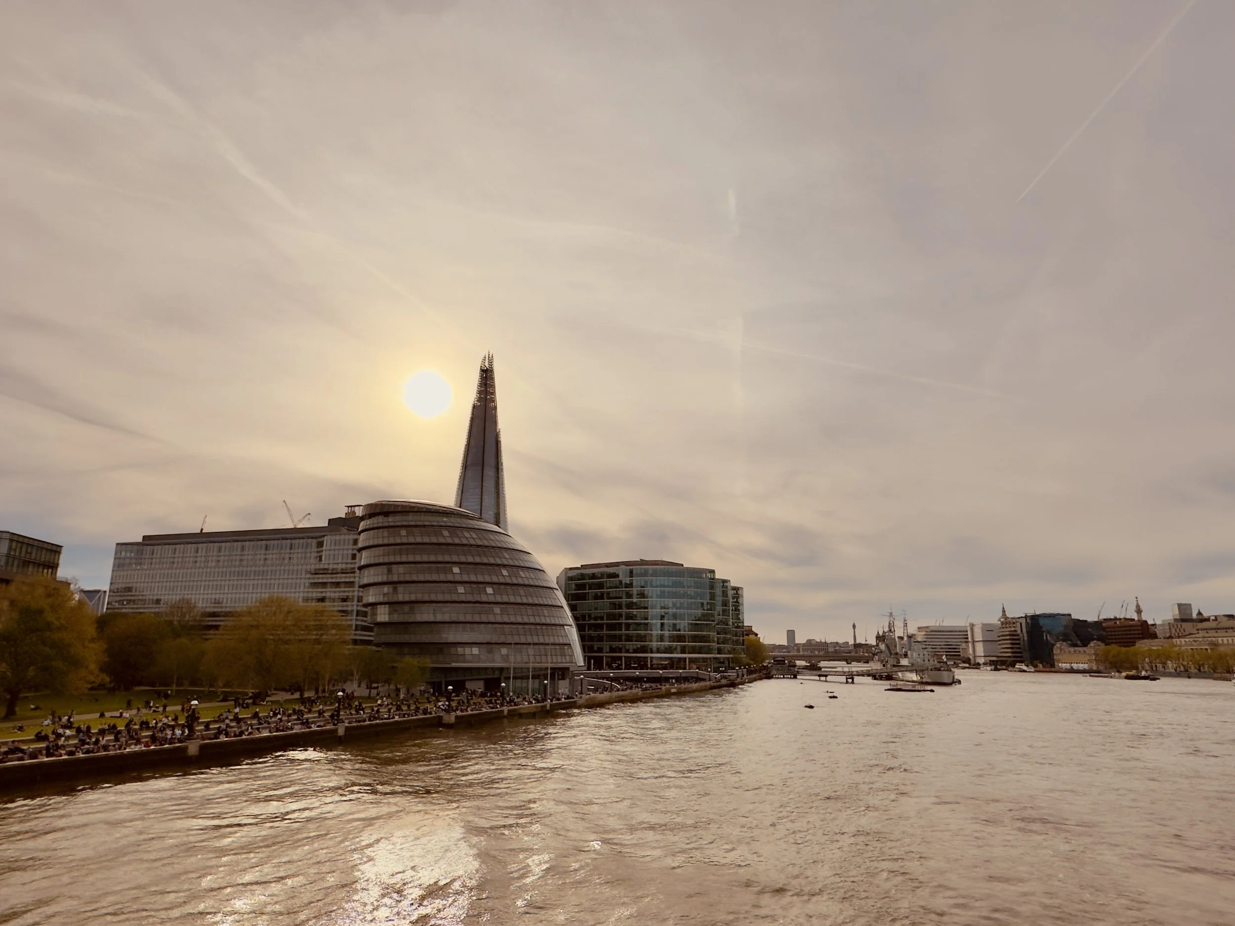 London skyline along the River Thames with modern buildings, including The Shard, and the sun in the sky.