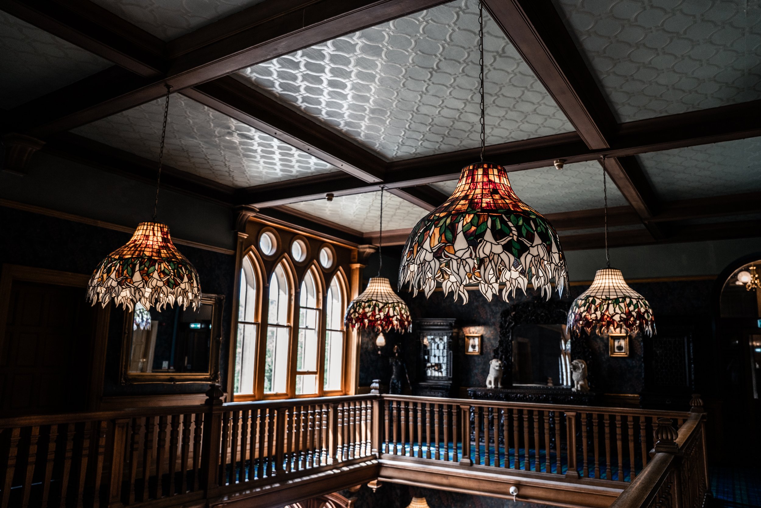 Multiple Tiffany-style stained glass pendant lamps hanging from the ceiling of a room with ornate woodwork and arched windows.