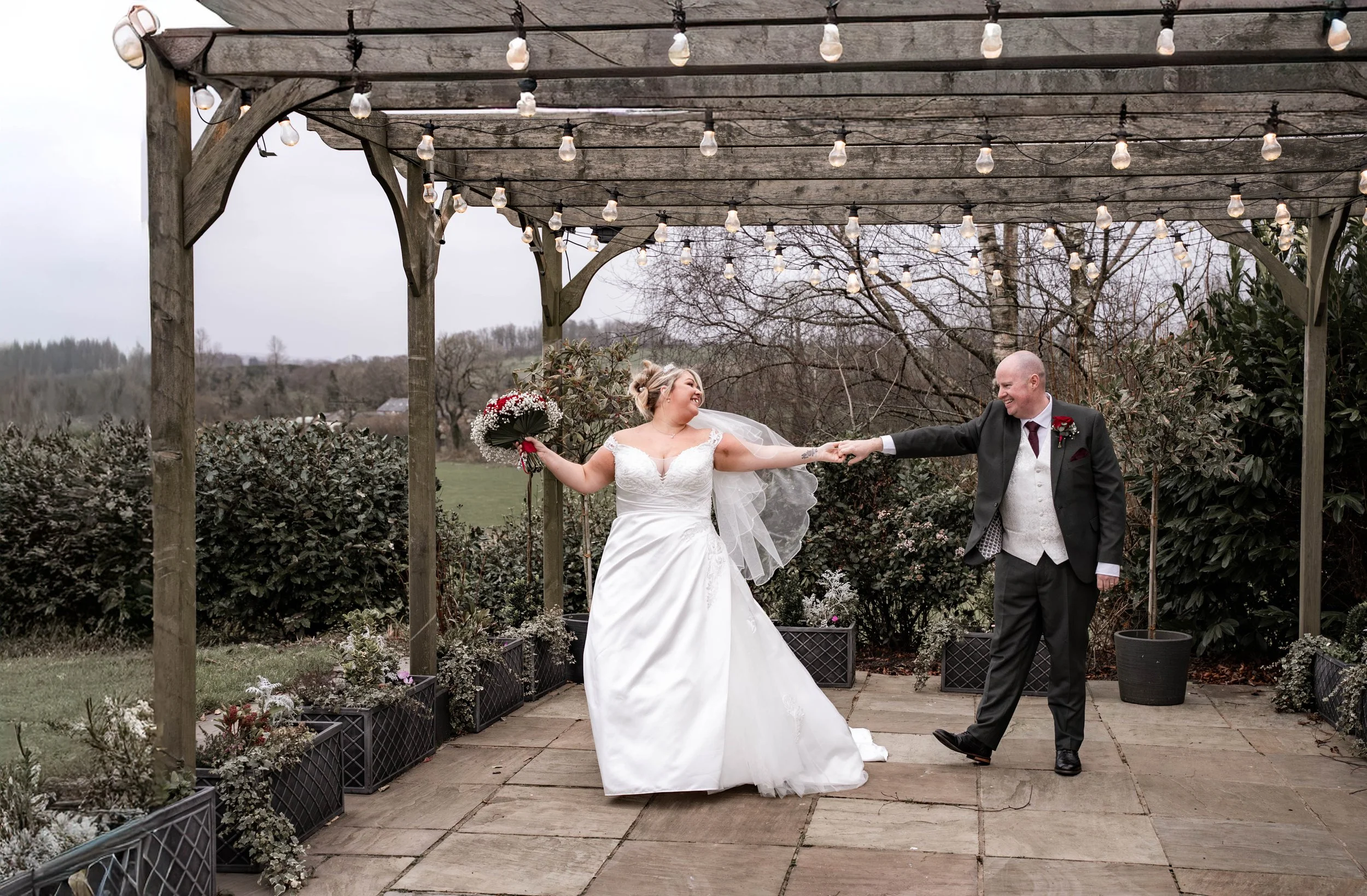 Bride and groom dancing outdoors under string lights with floral arrangements around.