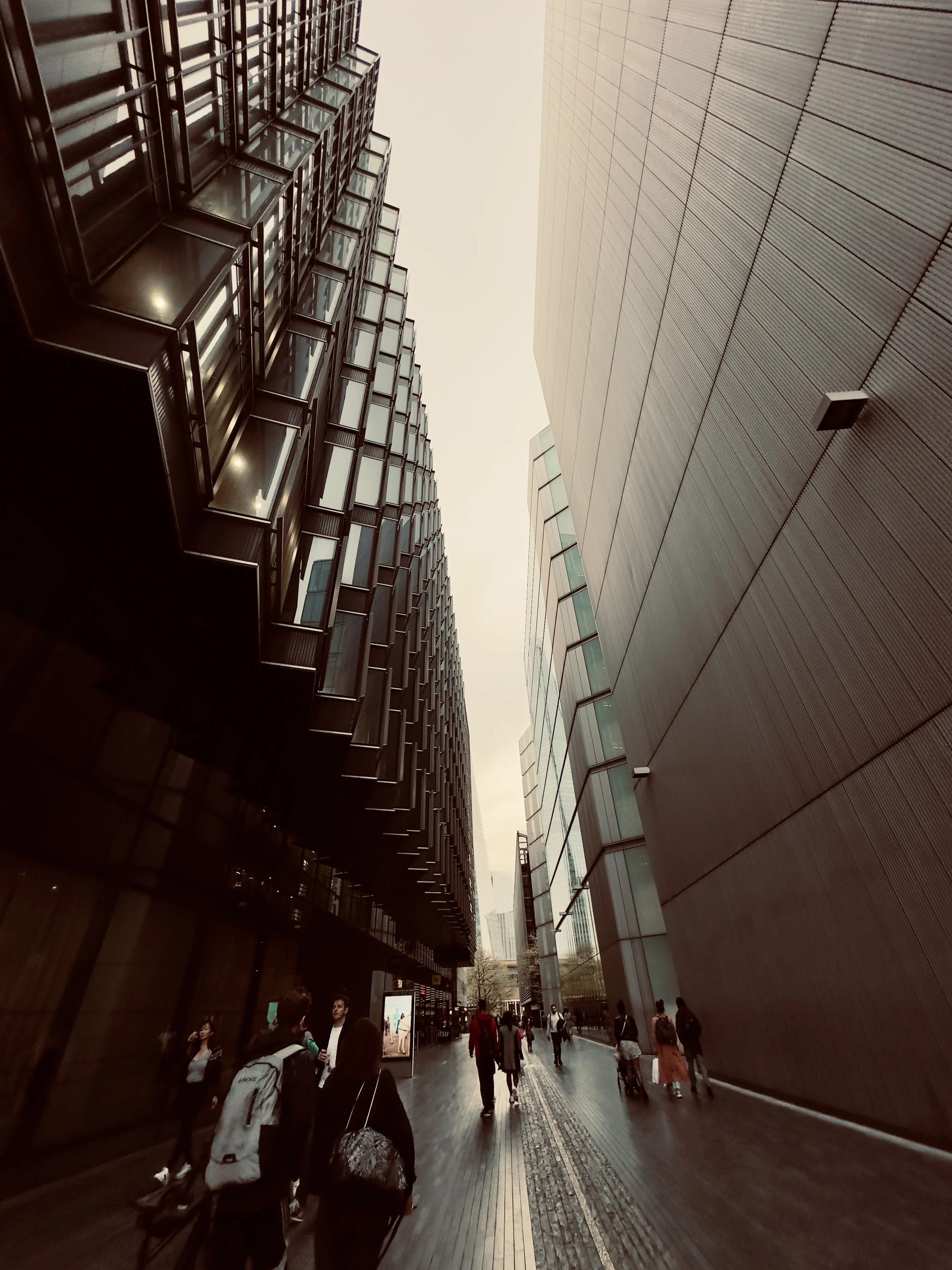 People walking on a city street between tall modern buildings with glass and metal facades.