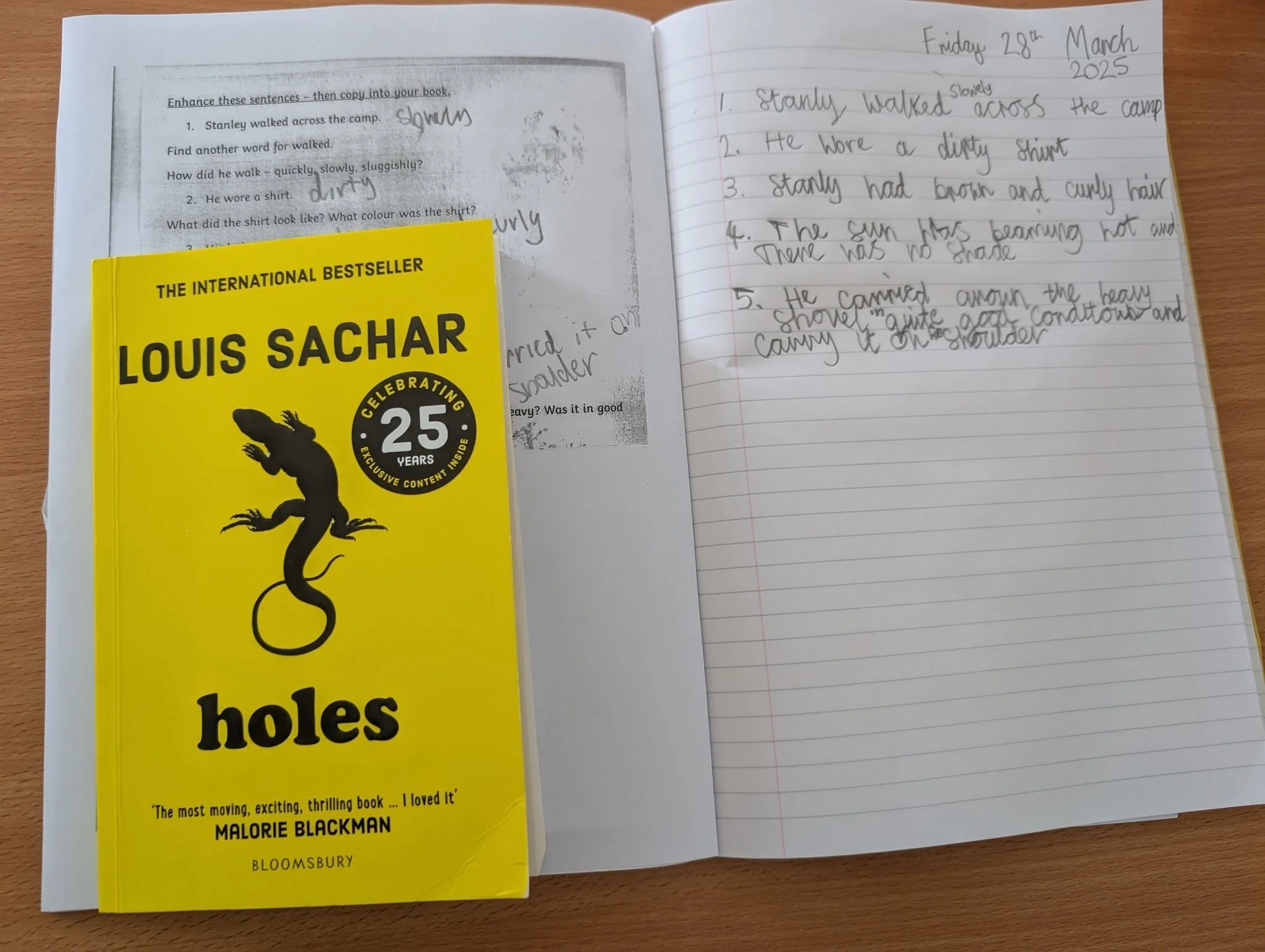 Open notebook and a yellow copy of the book "Holes" by Louis Sachar on a wooden table.