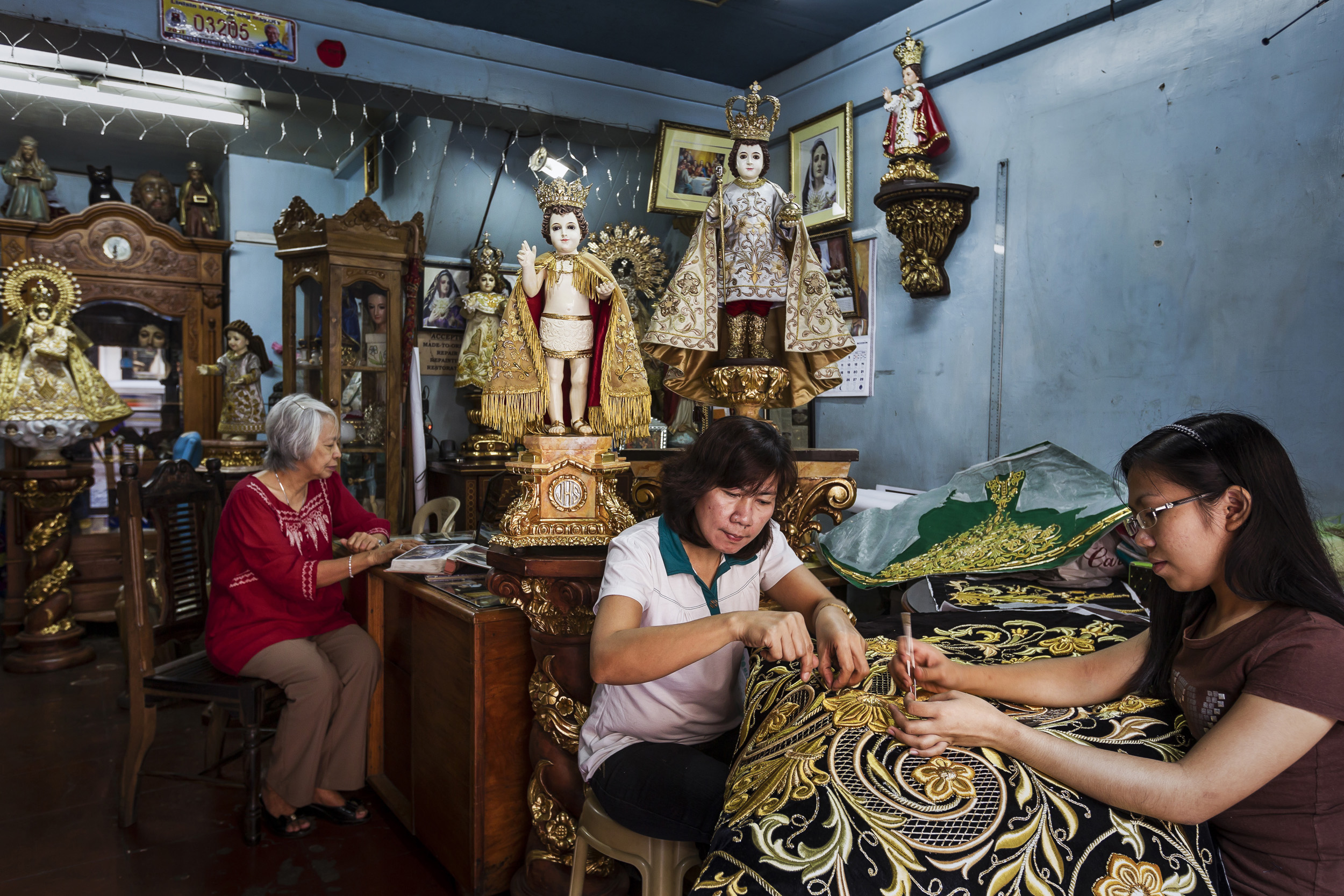 MANILA, PHILIPPINES, JANUARY 2012: Catholic icon dealer Nene Bernales and embroidery staff at work in her shop in Manila, Philippines, 25 January 2012. They are surrounded by Icons that have heads and hands made of Ivory. Nene's husband Marcial Bern