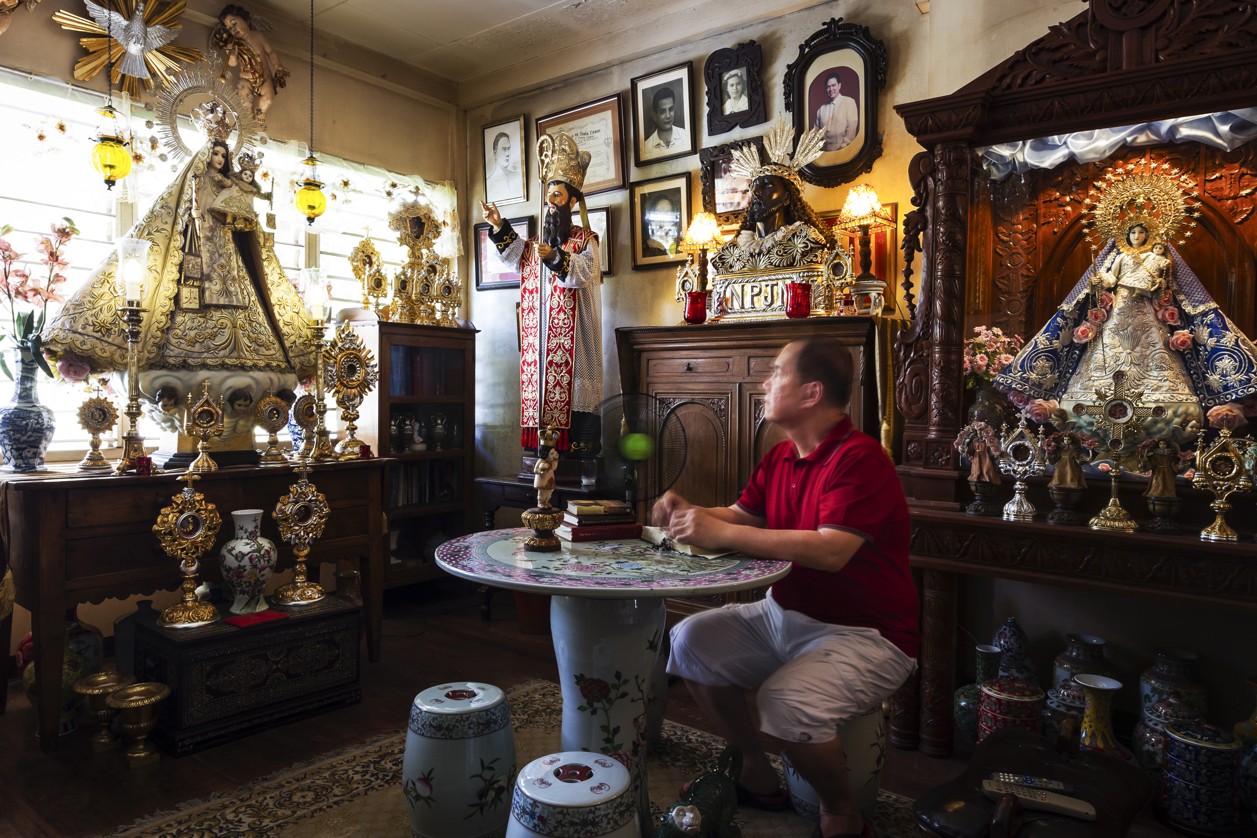 CEBU, PHILIPPINES, JANUARY 2012: A wealthy, devout Filipino man reads his bible study and cleans his religious icon collection which is largely carved out of Ivory, Cebu, Philippines, January 19, 2012. This collection has both new and old pieces, so
