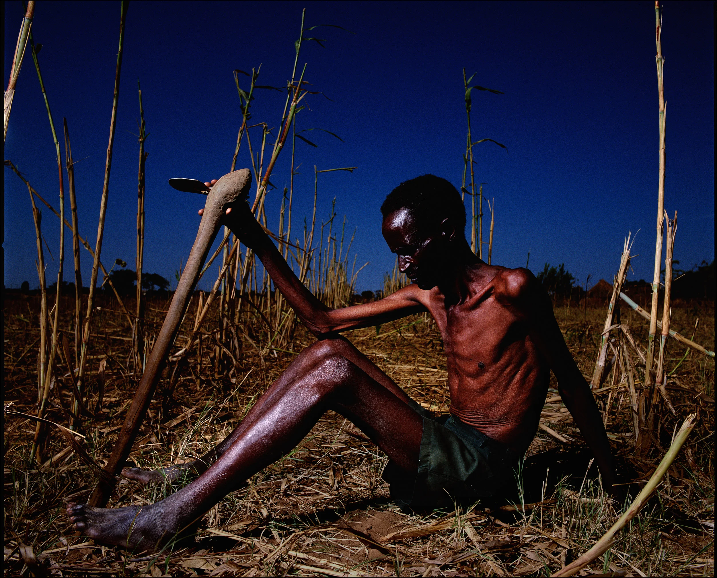 Northern Zambia, August 2003. Zambia enters its 6th year of severe drought. A starving farmers sits amongst the ruins of his failed crop. He is HIV+ and his malnutrition has greatly accelerated the decline of his immune system.
