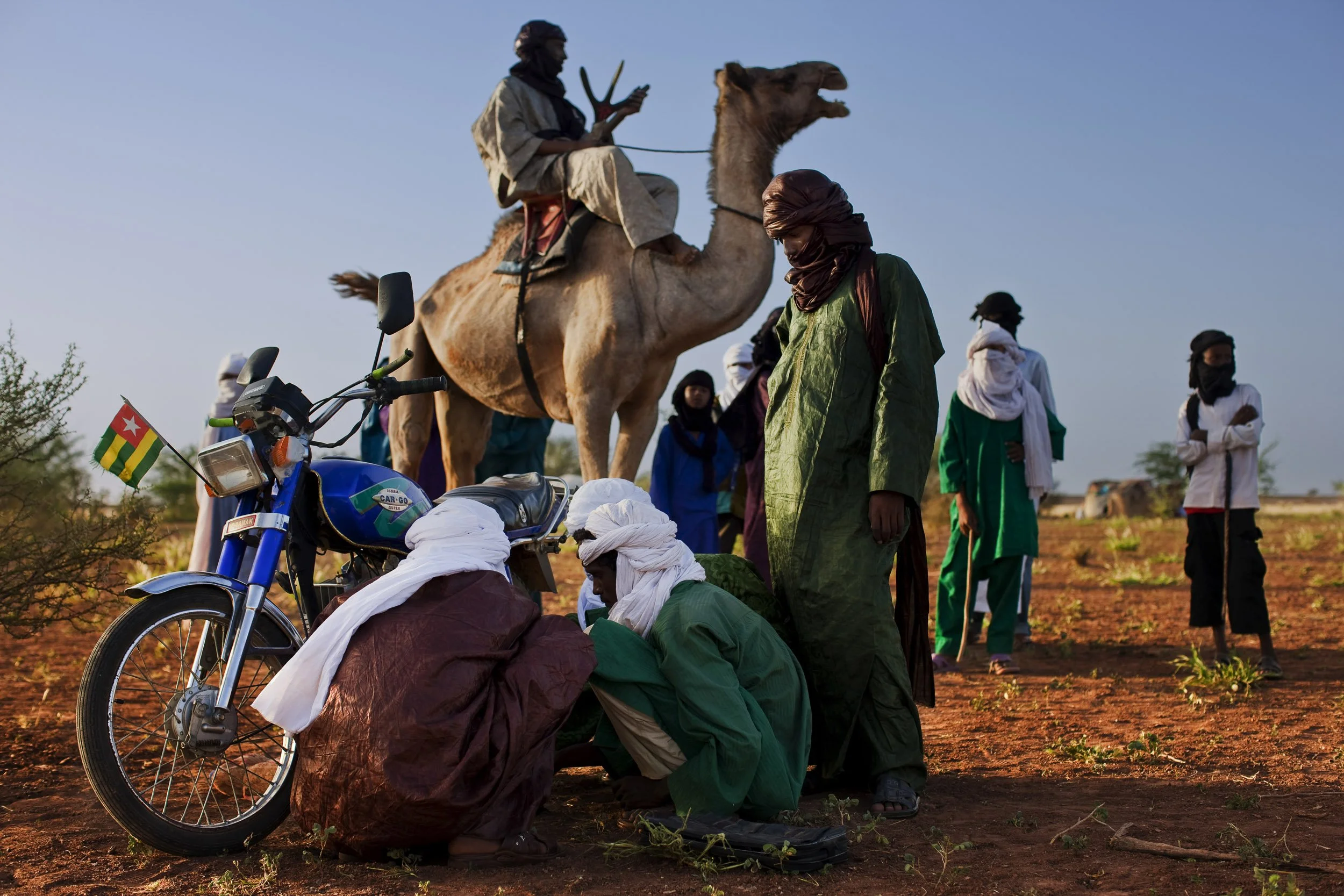 INGAL, NIGER, OCTOBER 2009: Tuareg men repair a small engined motorcycle in a Tuareg Nomad camp while a man on the more traditional camel looks on, Ingal Region, Niger, 09 October 2009. Motorbikes have become the emergency vehicle of the Tuareg noma