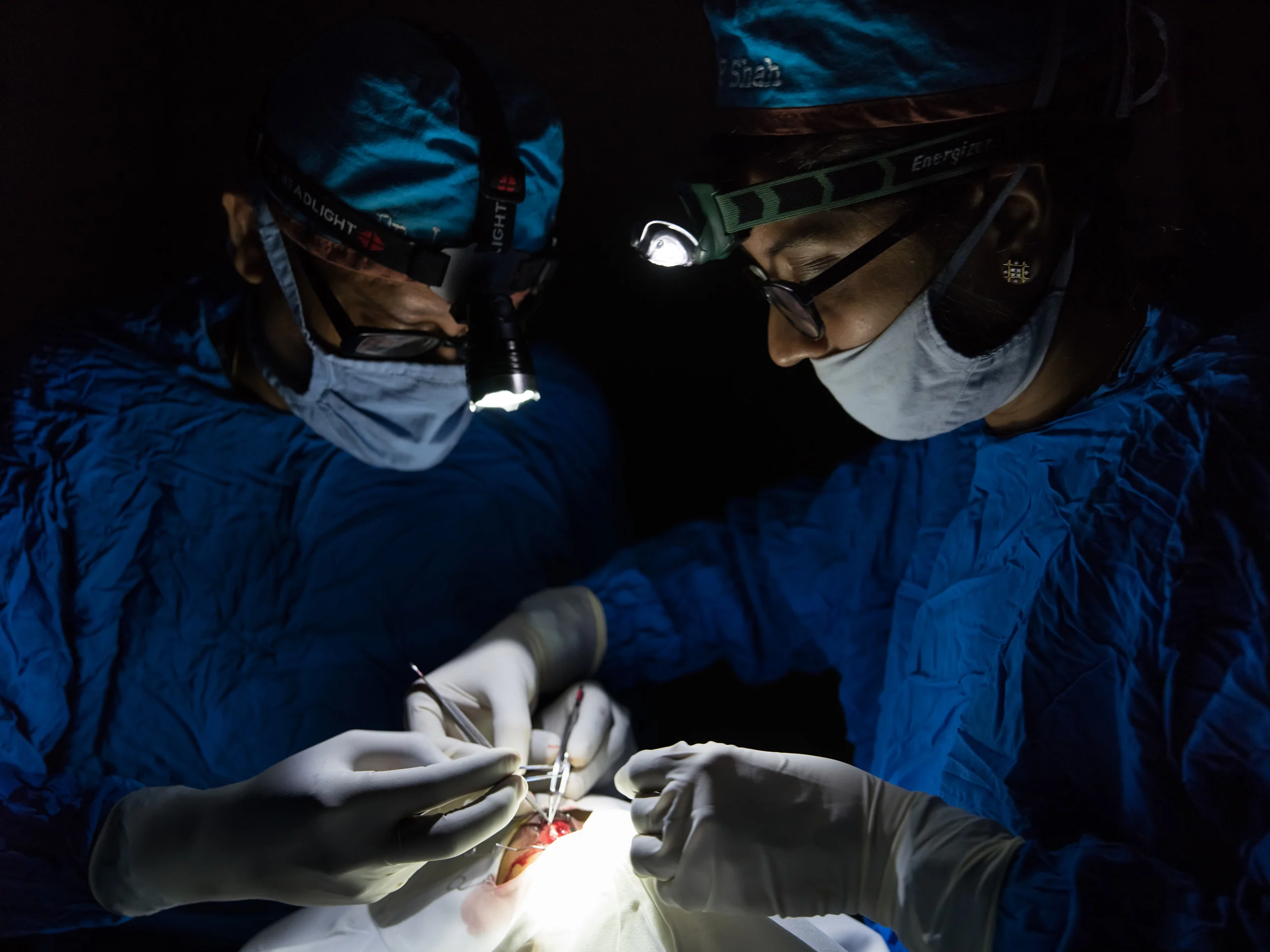 SHRI BHOJAY SARVODAYA EYE HOSPITAL, BHUJ, KUTCH, INDIA, JULY 22 2015: Eye surgeons Janak and Preeti Shah working via headlamp on a surgical operation during a powercut in this remote region of India. Dr Janak Shah is an accomplished and prolific eye