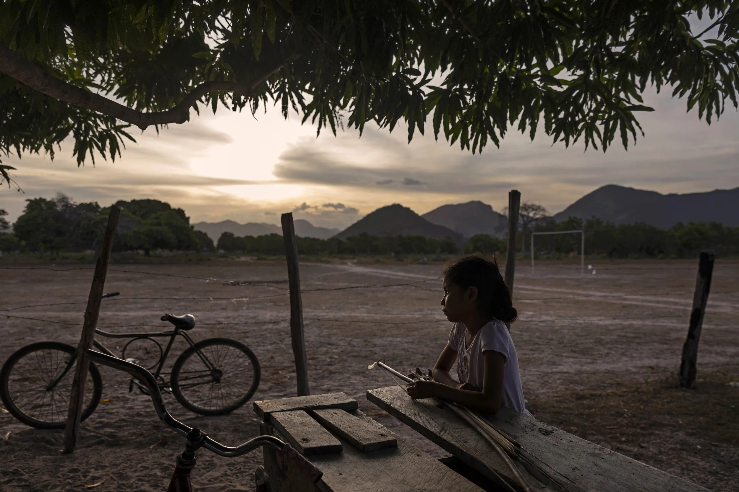KARASABAI, SOUTH PAKARAIMAS, GUYANA: Sherika Khan sits outside at a table with her father’s hunting bow and arrows next to her. She is waiting to say goodbye to him before he goes huniting that night. Egbert Khan, her father, is preparing to set out