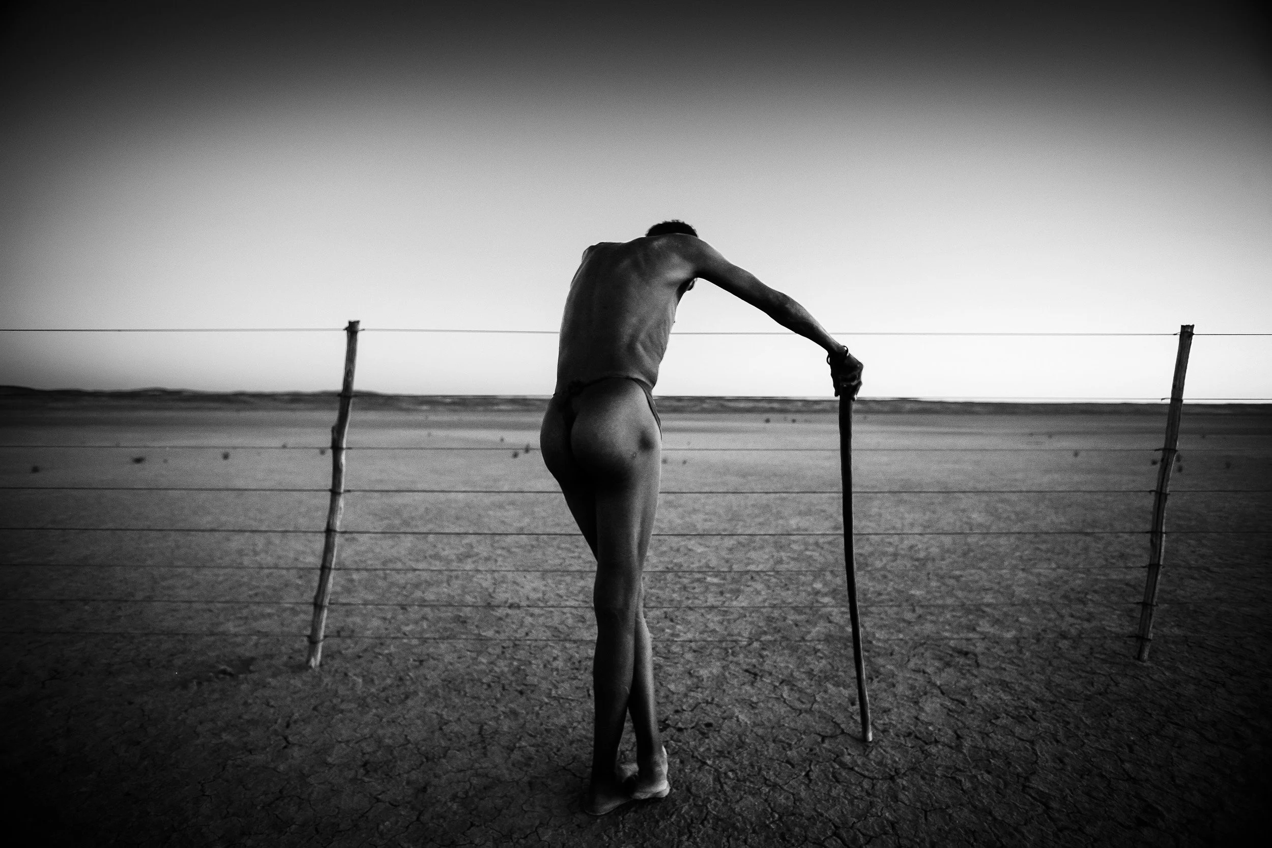 KALAHARI DESERT, SOUTH AFRICA: A San Bushman elder rests on a fence in the Kalahari desert that divides what used to be traditional bushmen land and is now mining territory. The San community says that access to water holes and traditional hunting a