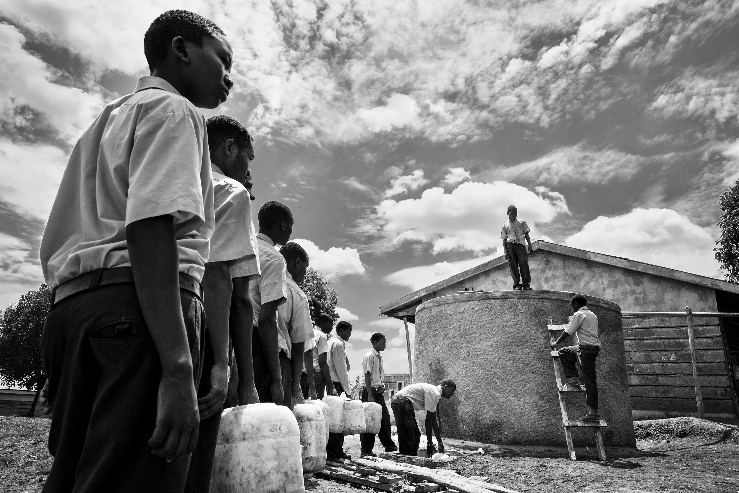 KISUMU, KENYA: Boys at a high school in rural Kenya queue up with water containers to receive water from their schools new water tank, Kisumu, Kenya. Access to a regular and clean water source makes for a far less disruptive school experience for st