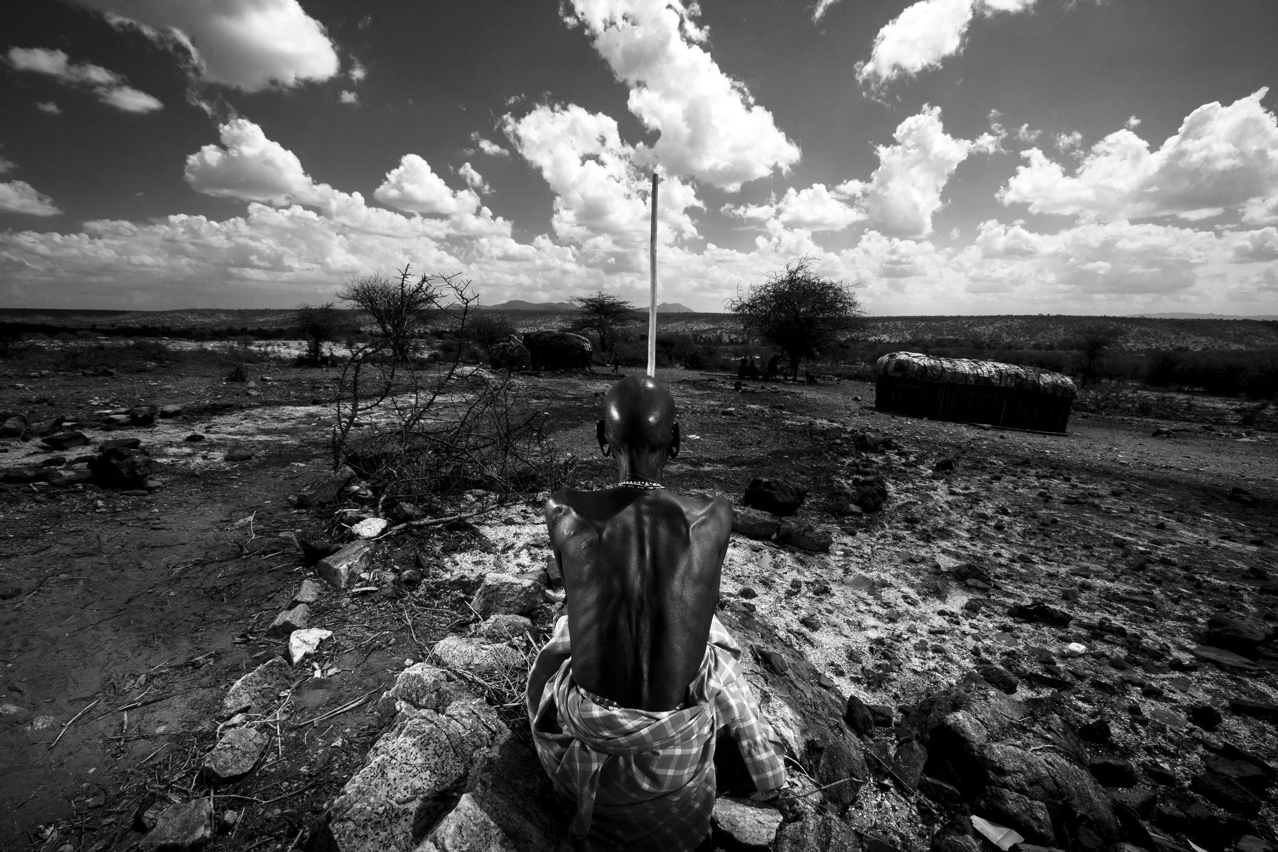 Kenya: A Masaai elder sits in the remains of his burned out shamba, he has just burned the place down before he moves on. A terrible five year drought has killed most of his cattle and it is traditional to burn down their living area before moving o