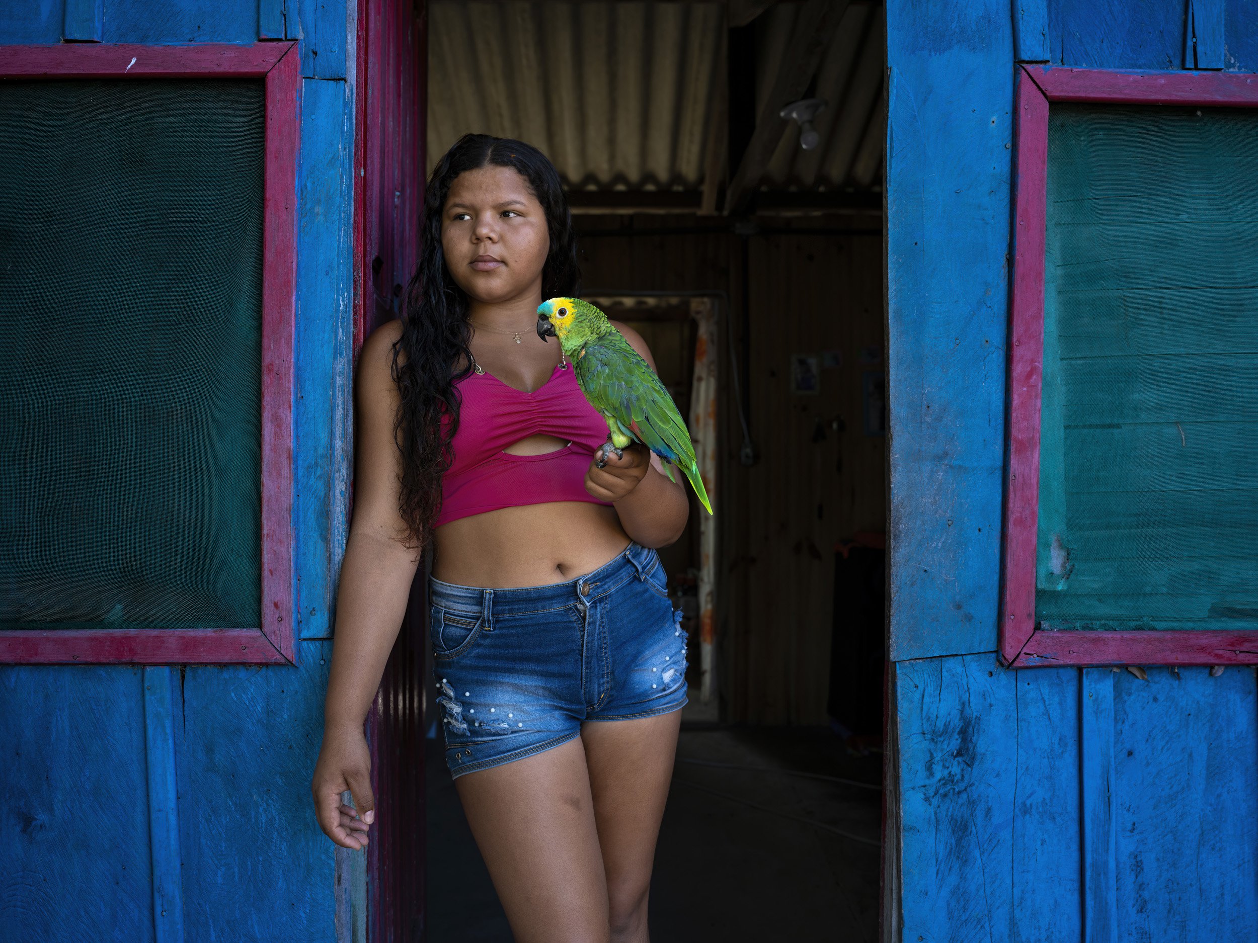Paraguay River, Matto Gross do Sul, Brazil: A young girl and her tame parrot in a simple fisherman's home on the Paraguay river in the early evening. Most of the people in this community used to live and work on cattle ranches inside the delta area