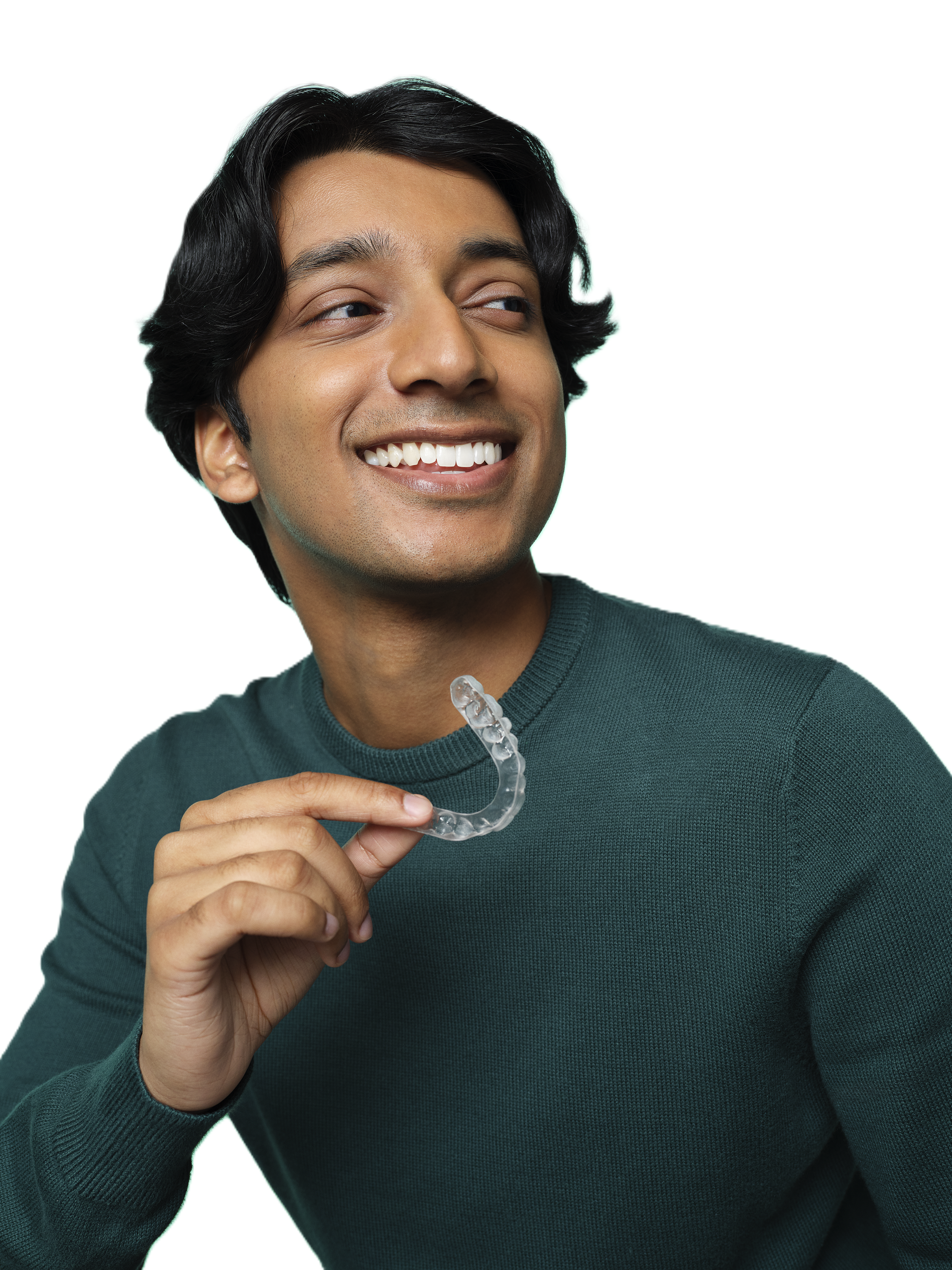 A young man with black hair smiling and holding a clear dental retainer in his right hand.
