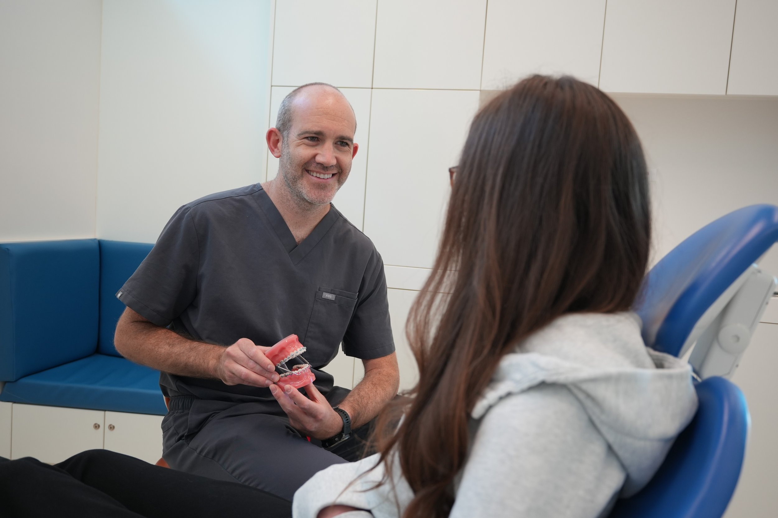 Dentist holding a dental model and explaining dental care to a female patient in dental office.