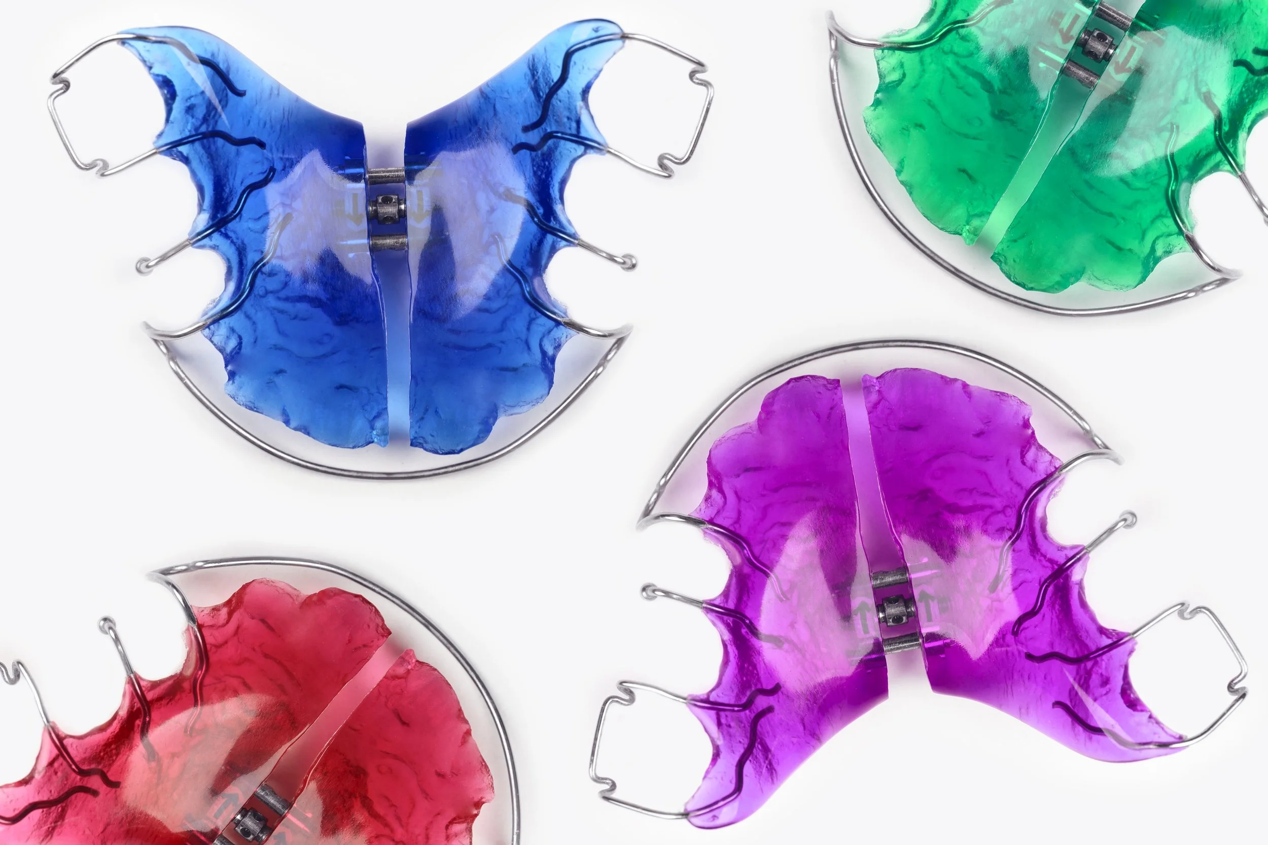 Four colorful retainers blue, green, red, and purple, each with clear plastic shields, arranged on a white background.