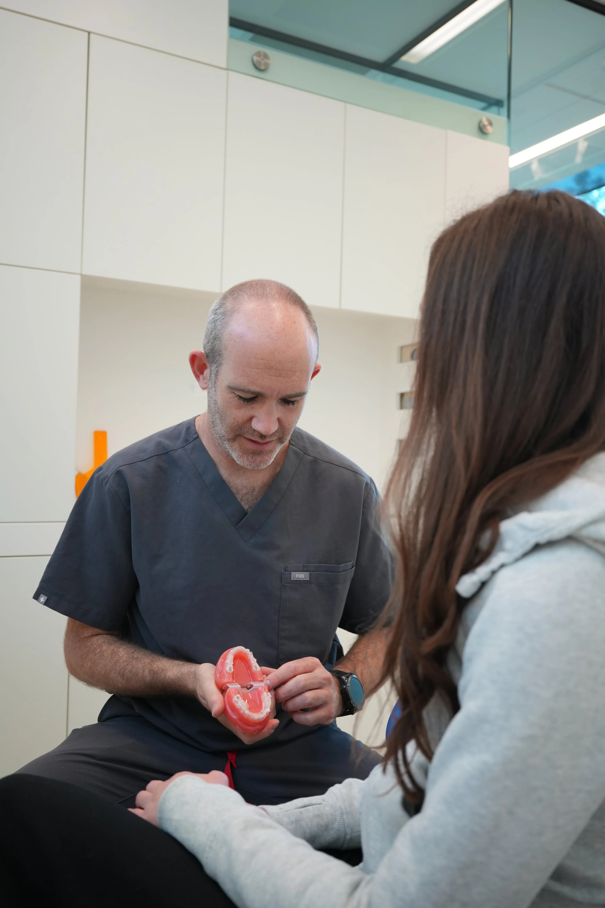 A dental professional showing a dental model of teeth to a patient in a clinical setting.