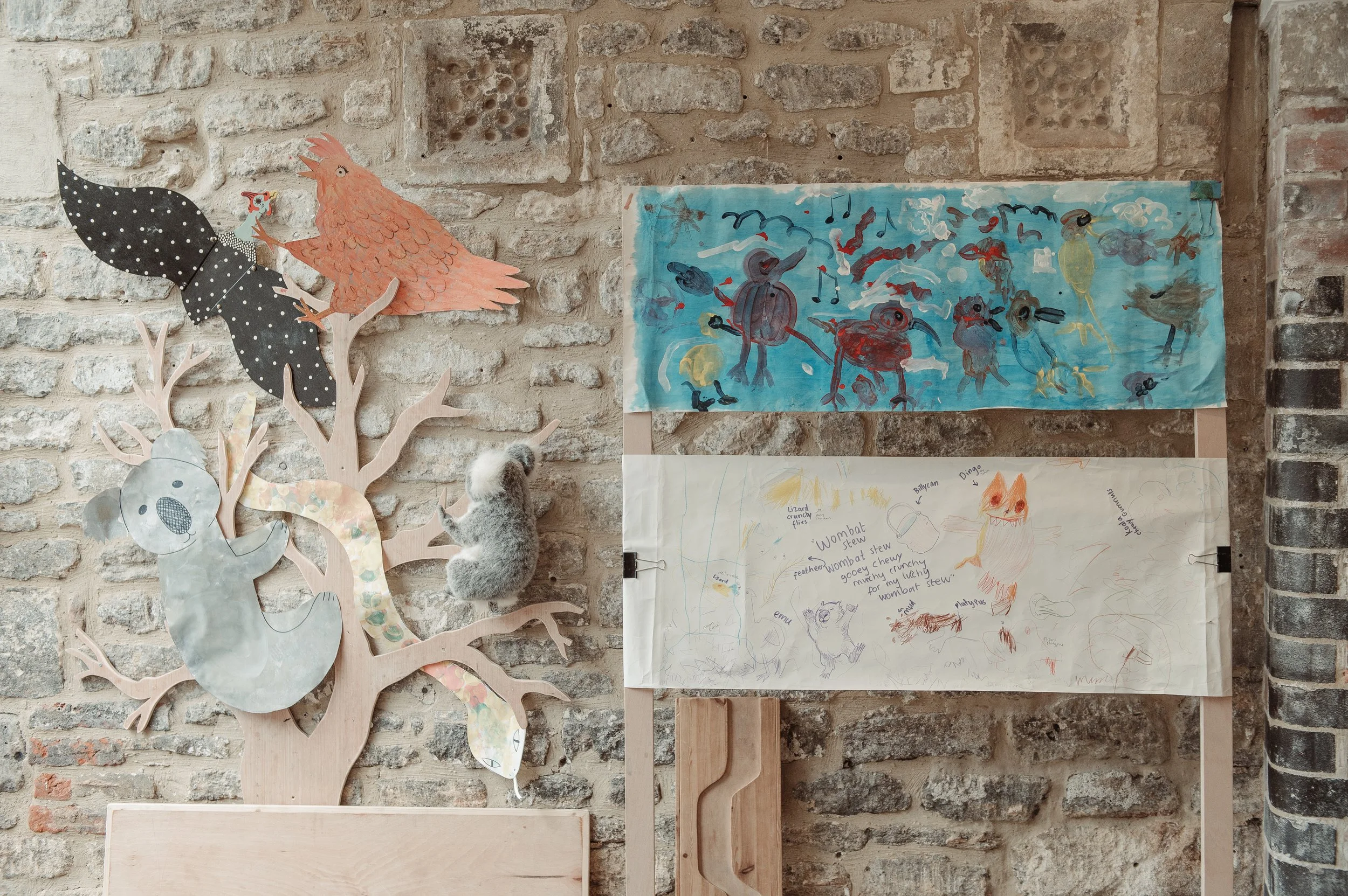 Decorative wall with paper art and children's artwork featuring animals and robots, mounted on a brick wall.