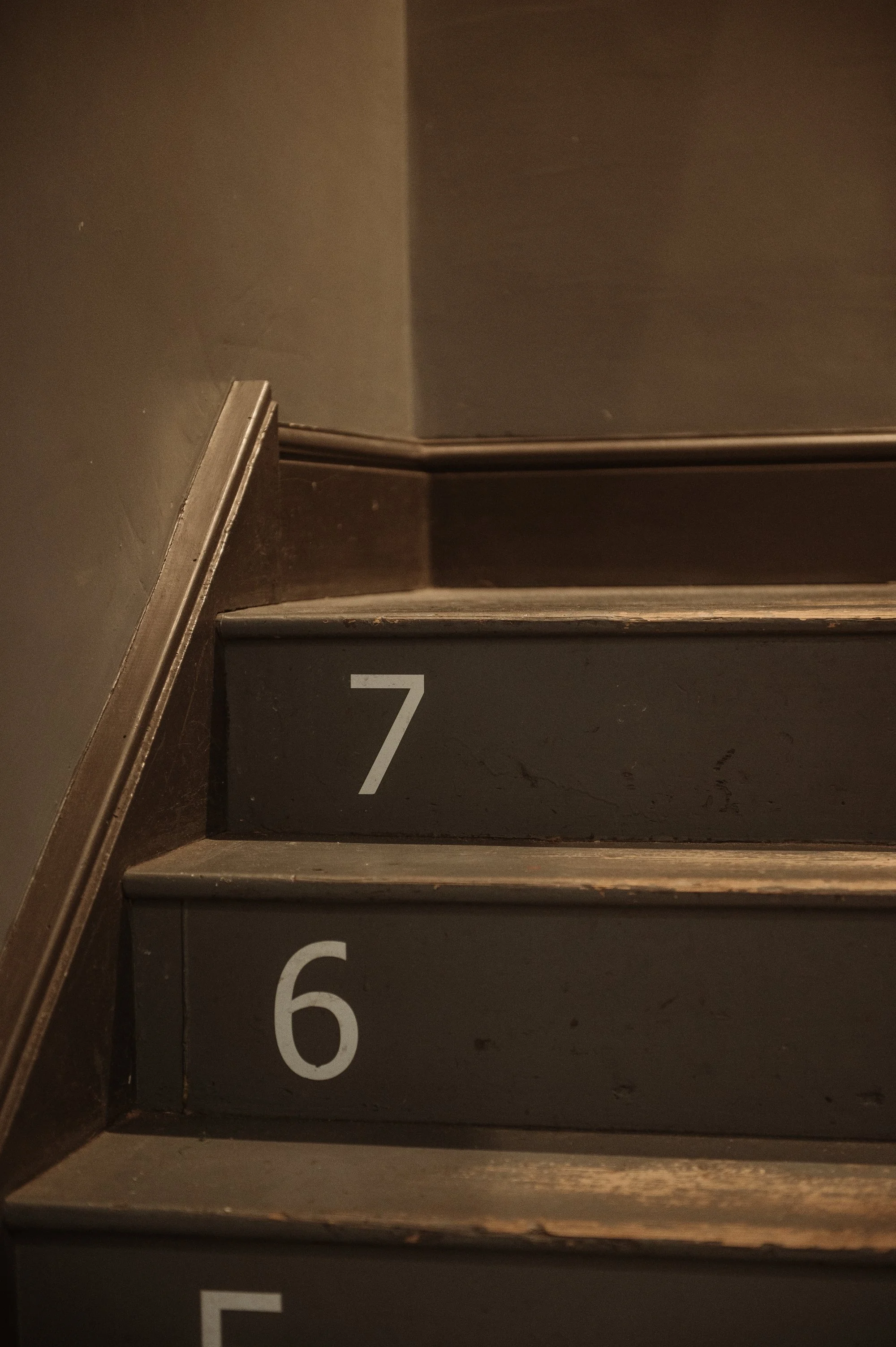 Close-up of stairs numbered 6 and 7 with dark-colored treads and a wooden handrail.