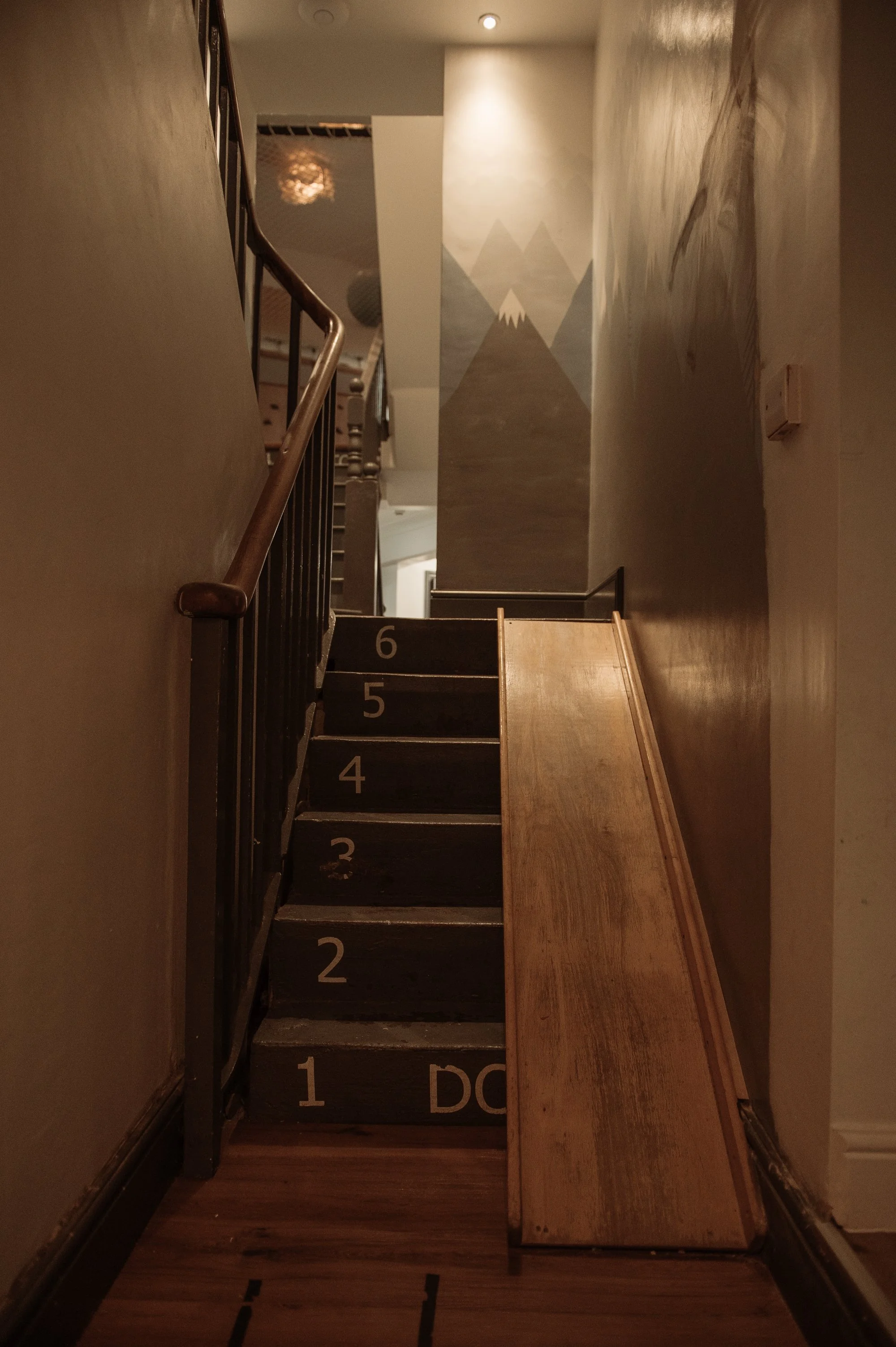 Indoor staircase with numbered steps from 1 to 6, with an accessible ramp on the right, leading up to a mural of mountains painted on the wall at the top of the stairs.