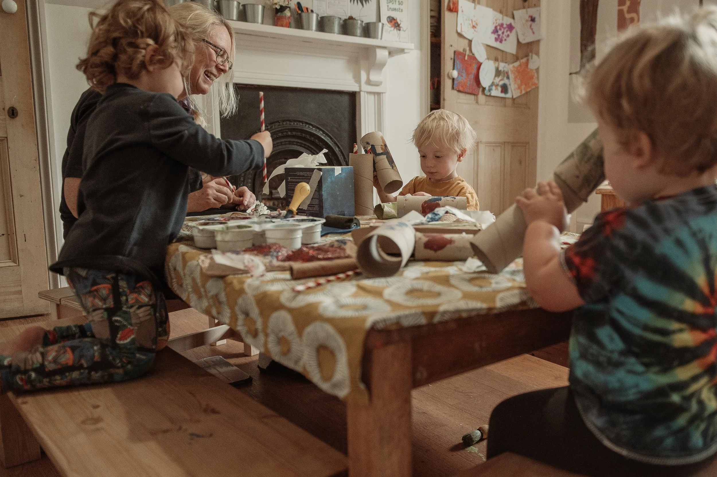 Children and adults gathered around a table engaged in holiday crafts, with wrapping paper and art supplies on the table.