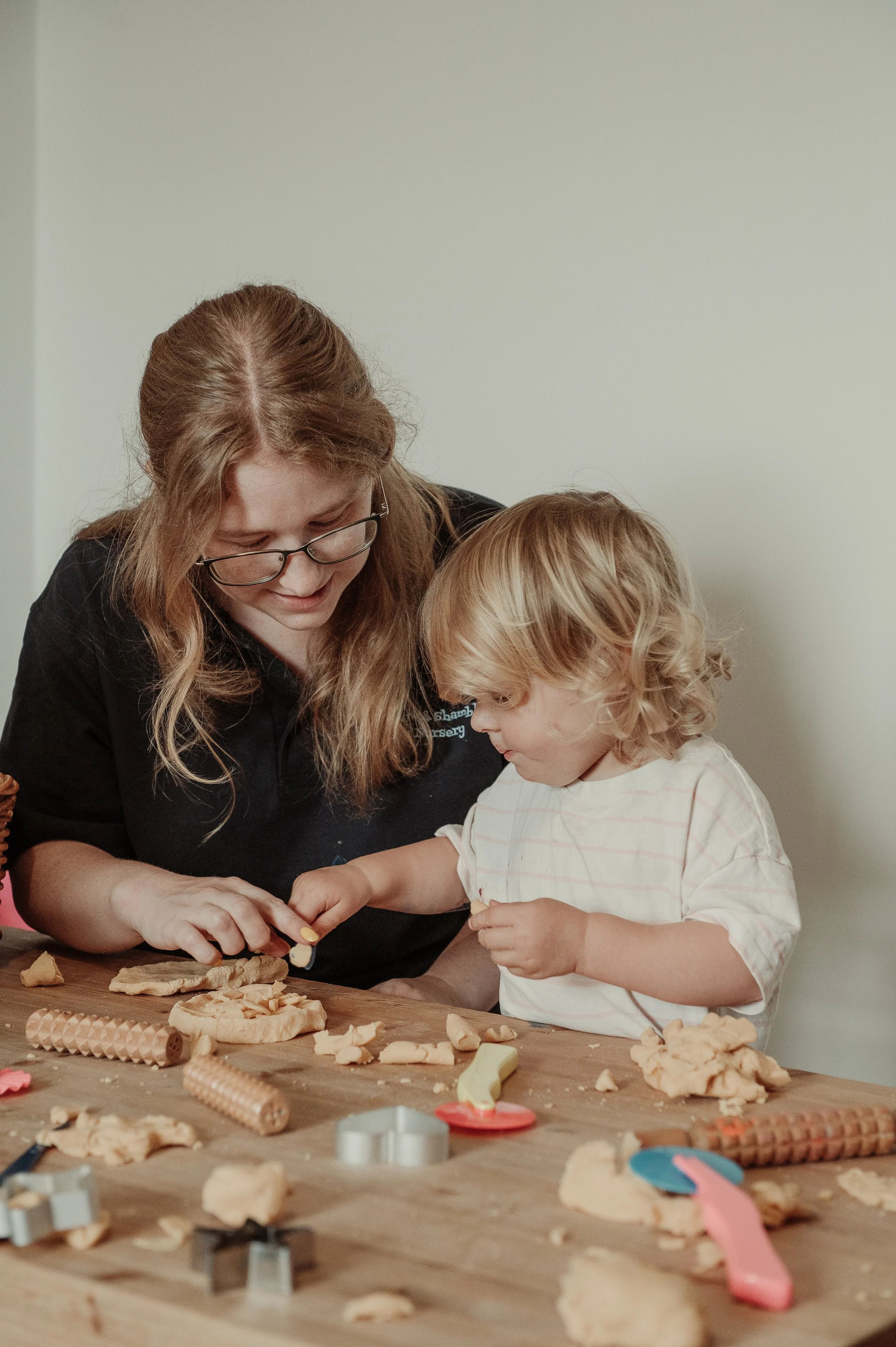 A woman and a young child playing with cookie dough and cookie cutters at a table.