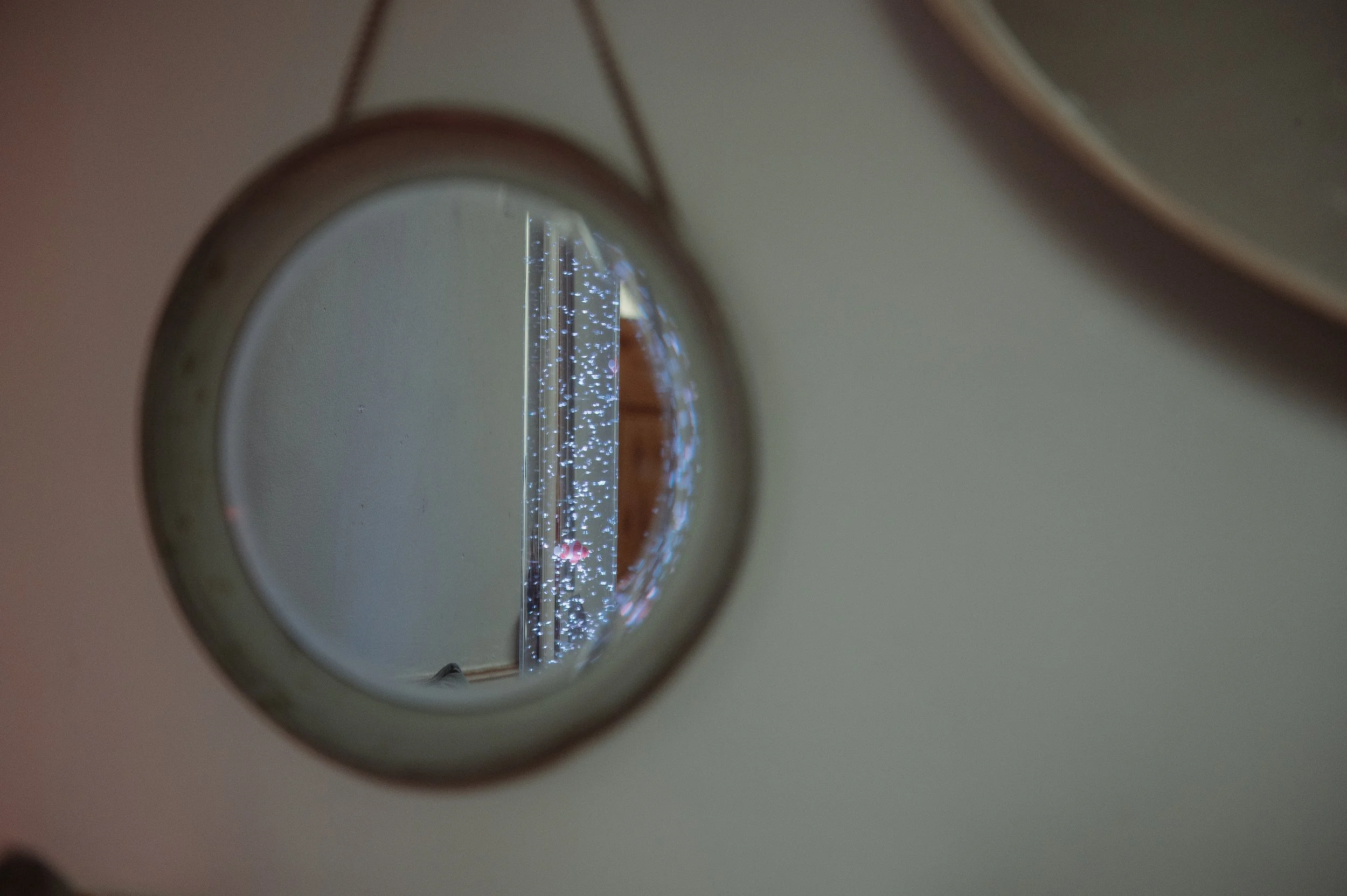 A circular mirror mounted on a wall, reflecting a string of blue and white fairy lights, with the wall and part of a wooden door frame visible in the background.