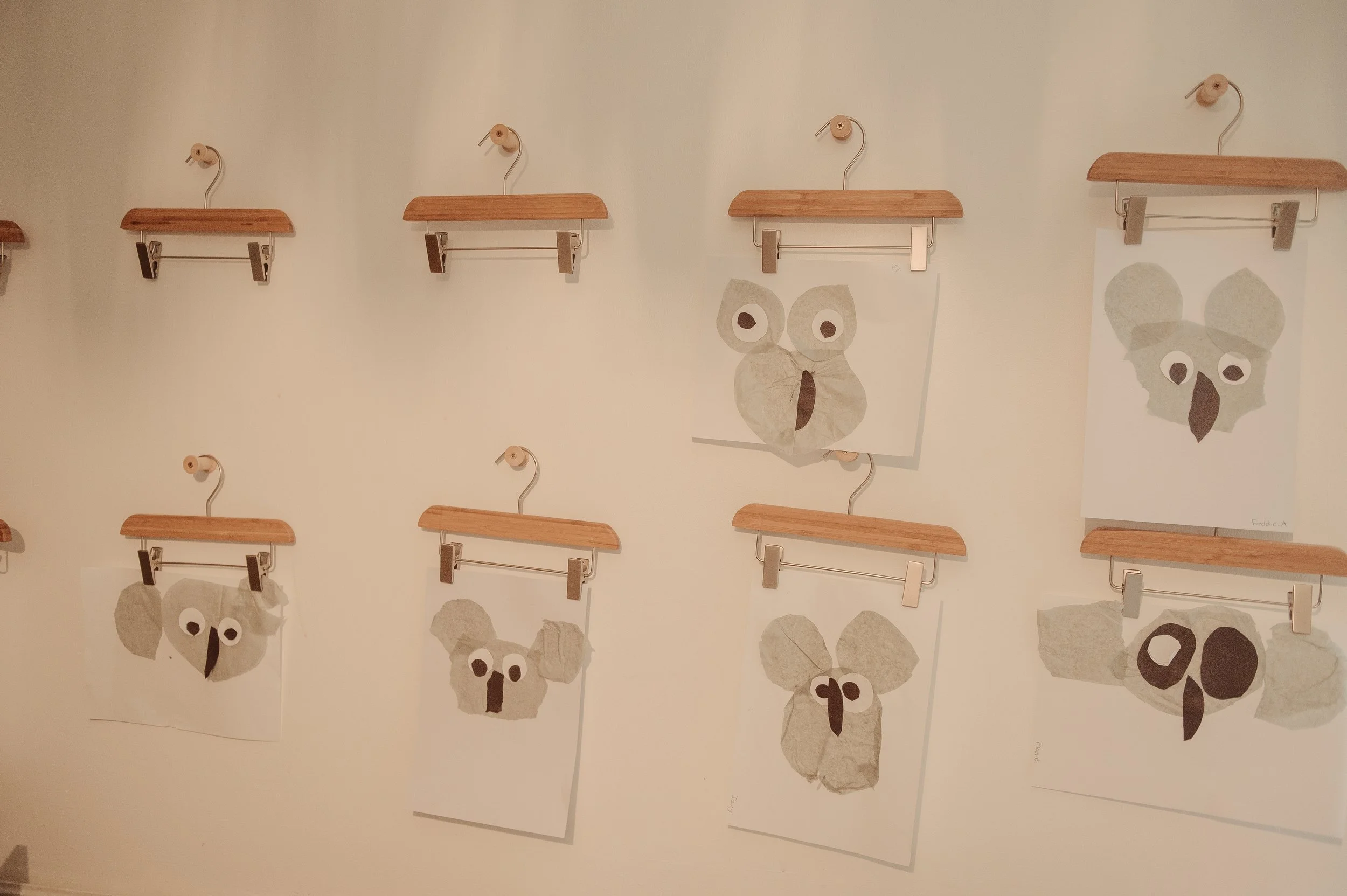Art display of paper collages depicting animal faces hung on a wall with wooden hangers.