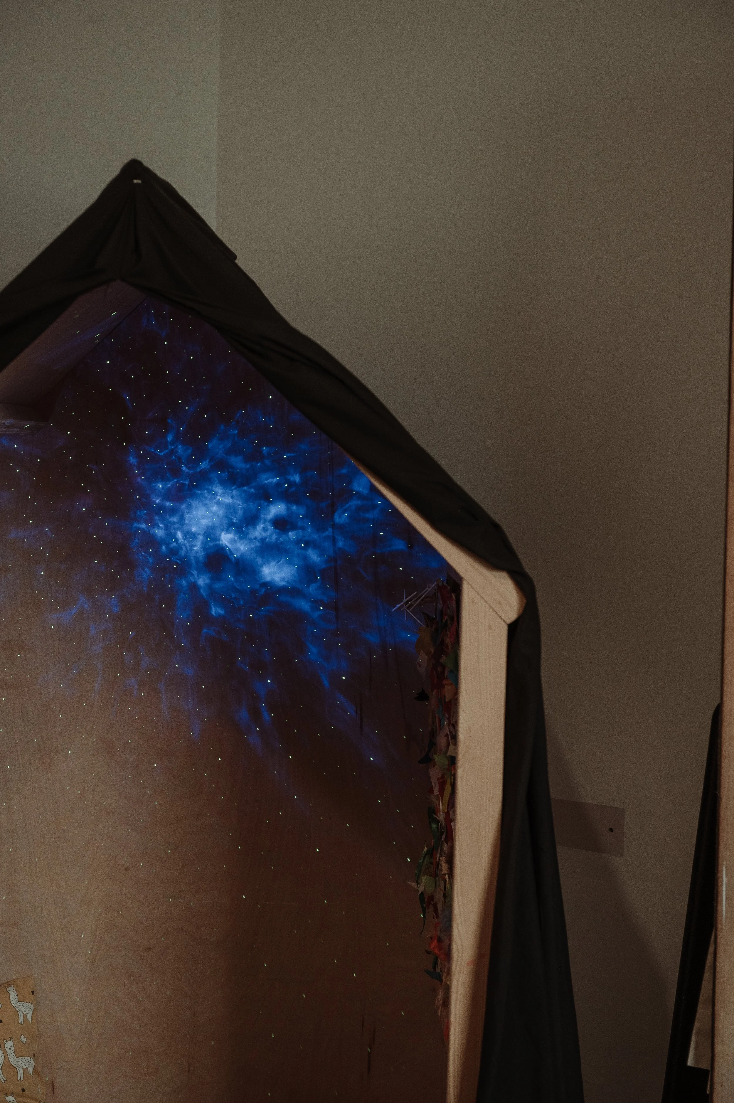 A wooden box with a dark fabric covering, displaying a starry sky with blue cosmic patterns on a screen inside