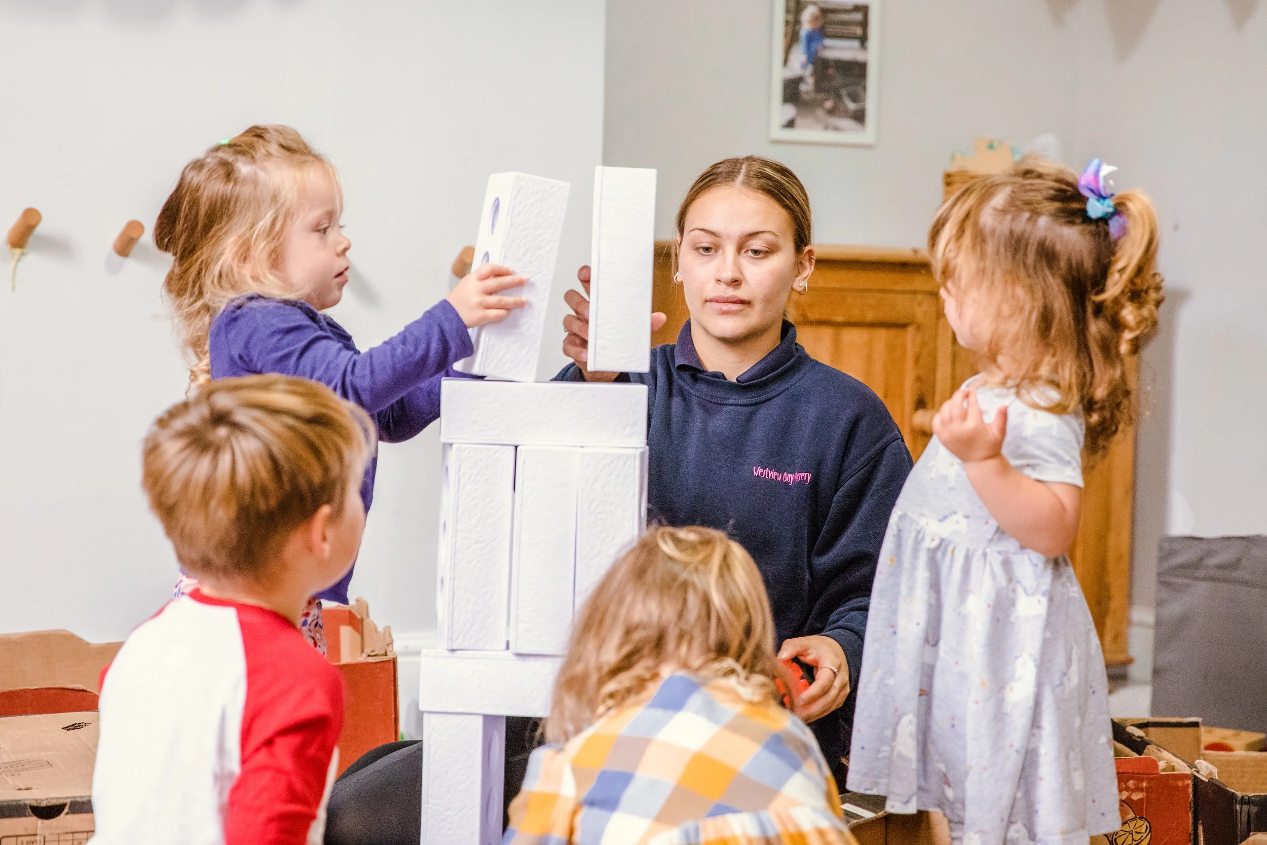 A woman and five children building with large white blocks in a room.