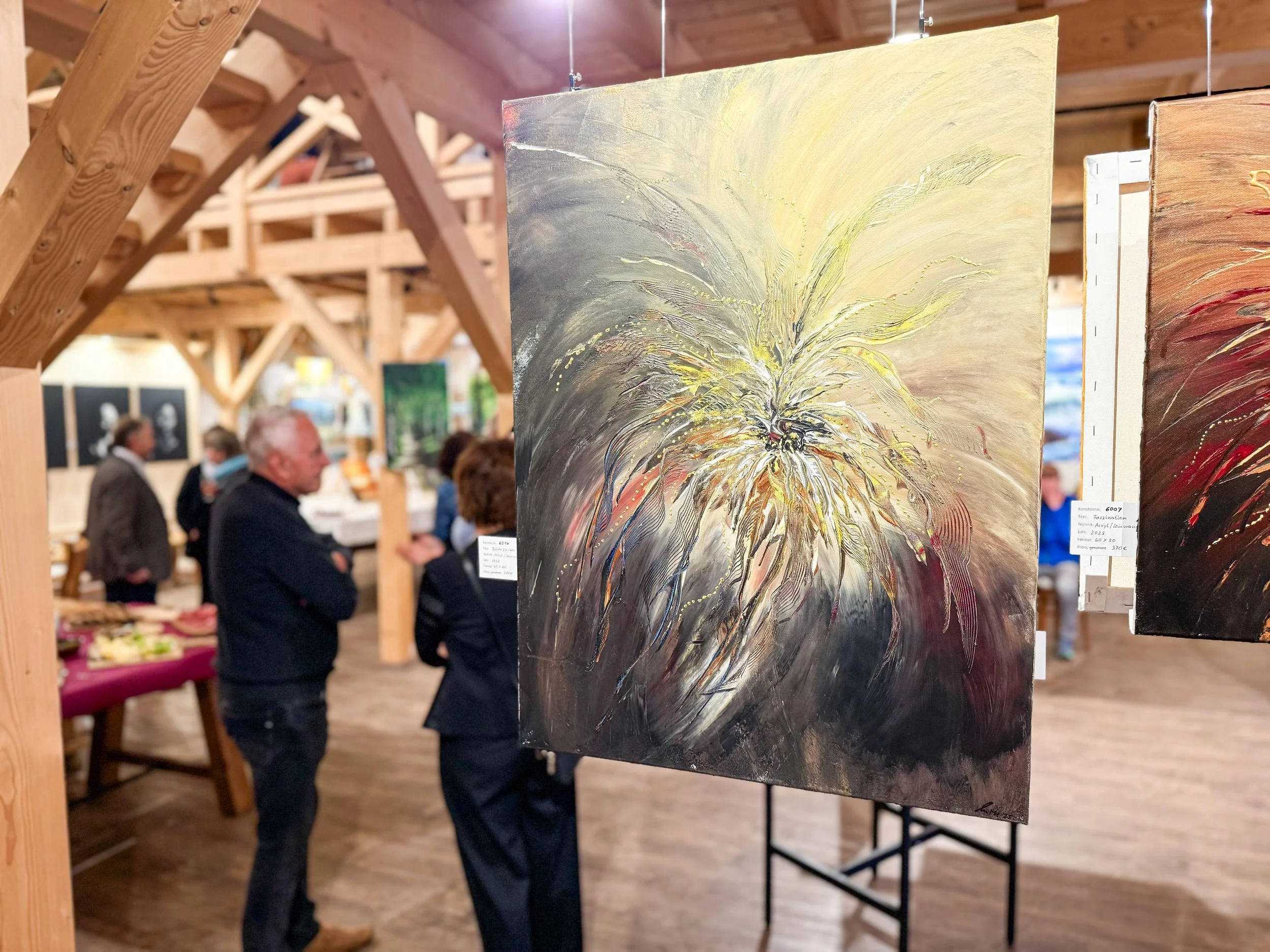 Abstraktes Gemälde mit hellen, dynamischen Pinselstrichen in Weiß, Gelb und Schwarz, präsentiert auf einer Kunstmesse in einem Holzgwinel mit mehreren Menschen im Hintergrund.