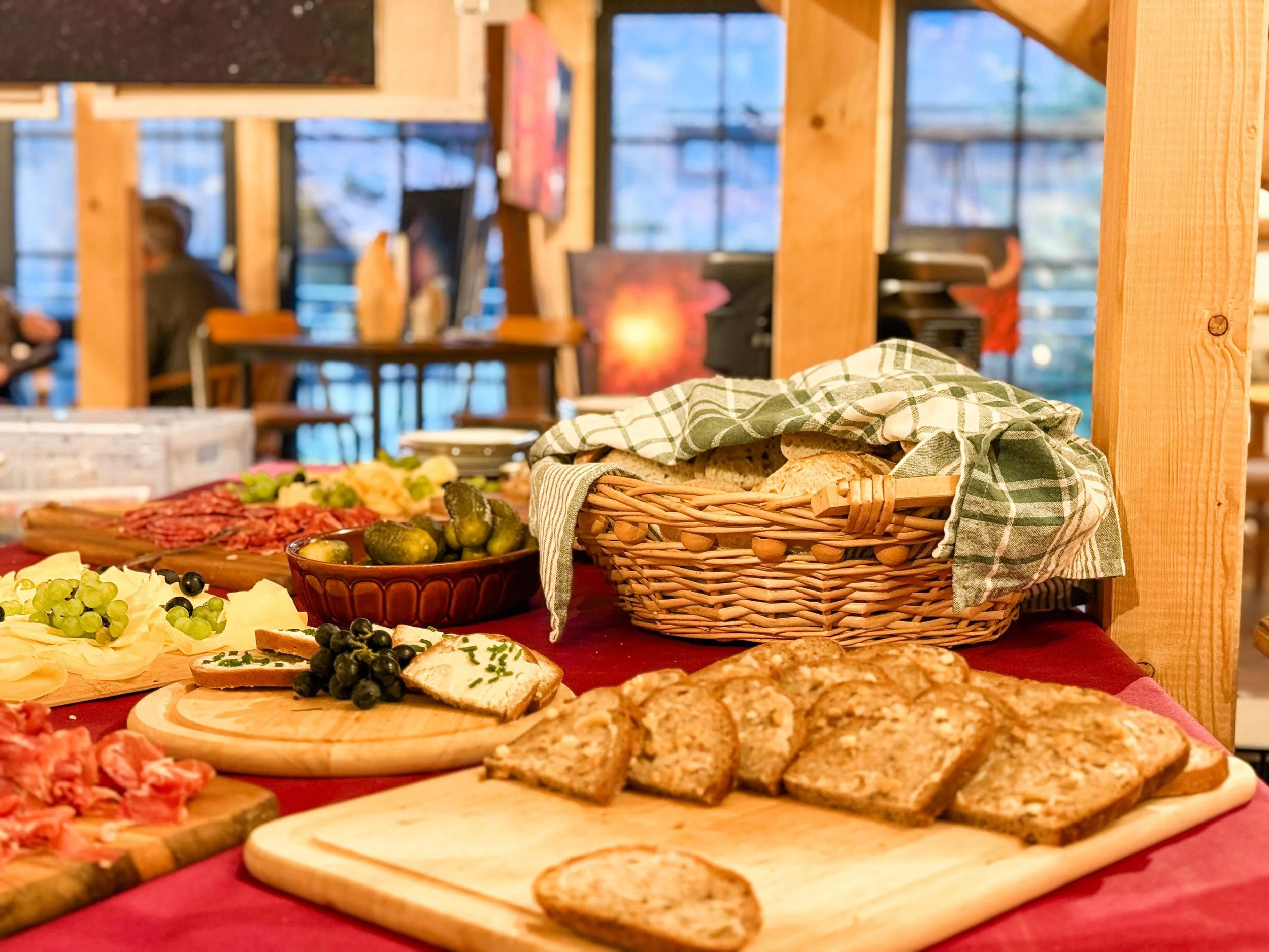 Brett mit verschiedenen Broten, Käse, Trauben, Cornichons und Aufschnitt in einer rustikalen Holzküche