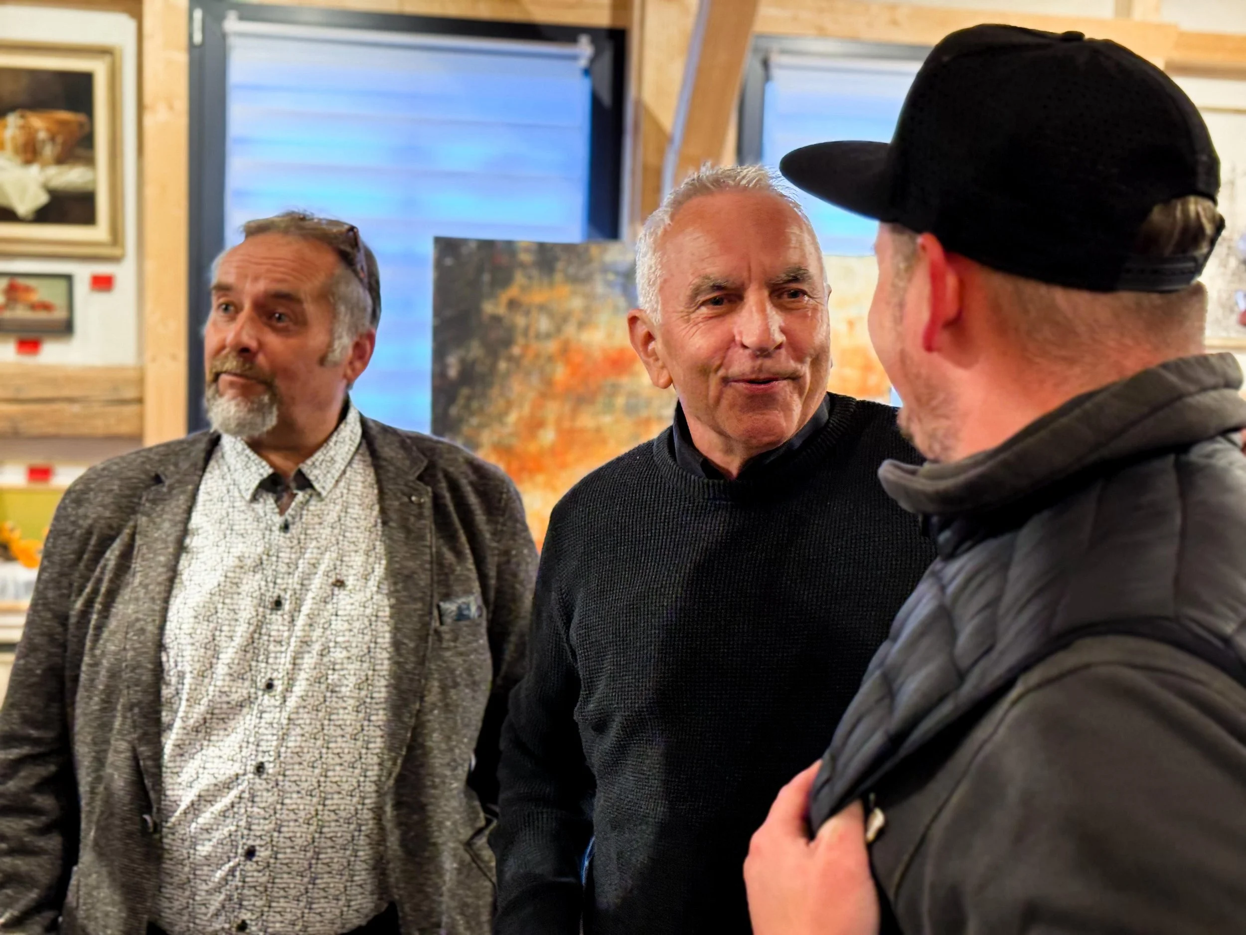 Drei Männer im Gespräch in einer Kunstgalerie.