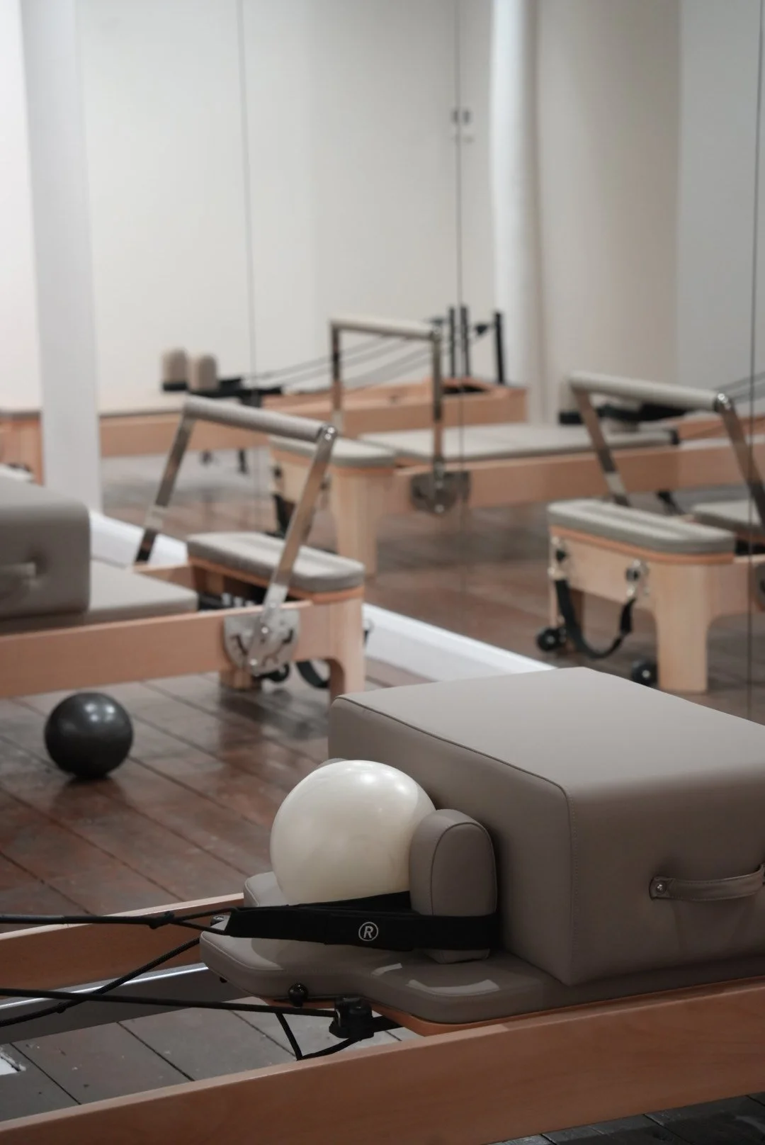 A Pilates studio with reformer machines and therapy balls, wood flooring, and a large mirror wall.