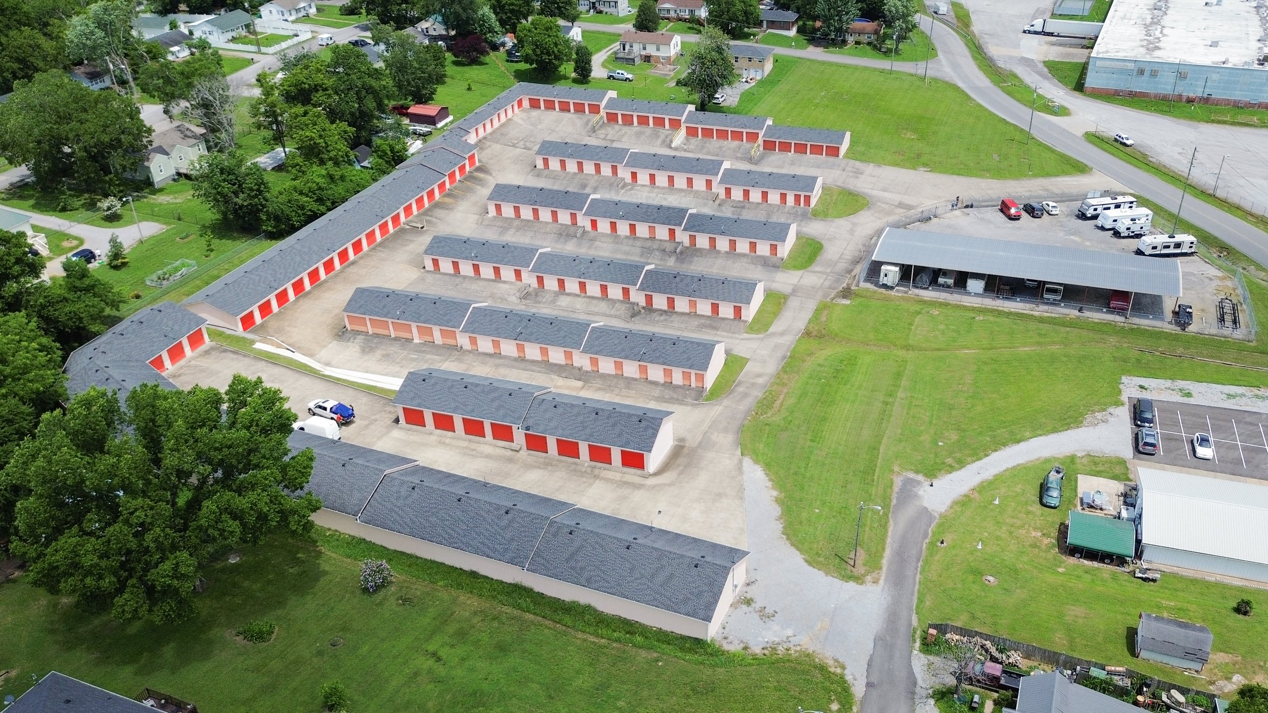 Aerial view of David Jent Mini-Storage facility with multiple rows of orange and white storage units, parking areas, and a large covered loading zone, surrounded by residential neighborhood with houses and green lawns.