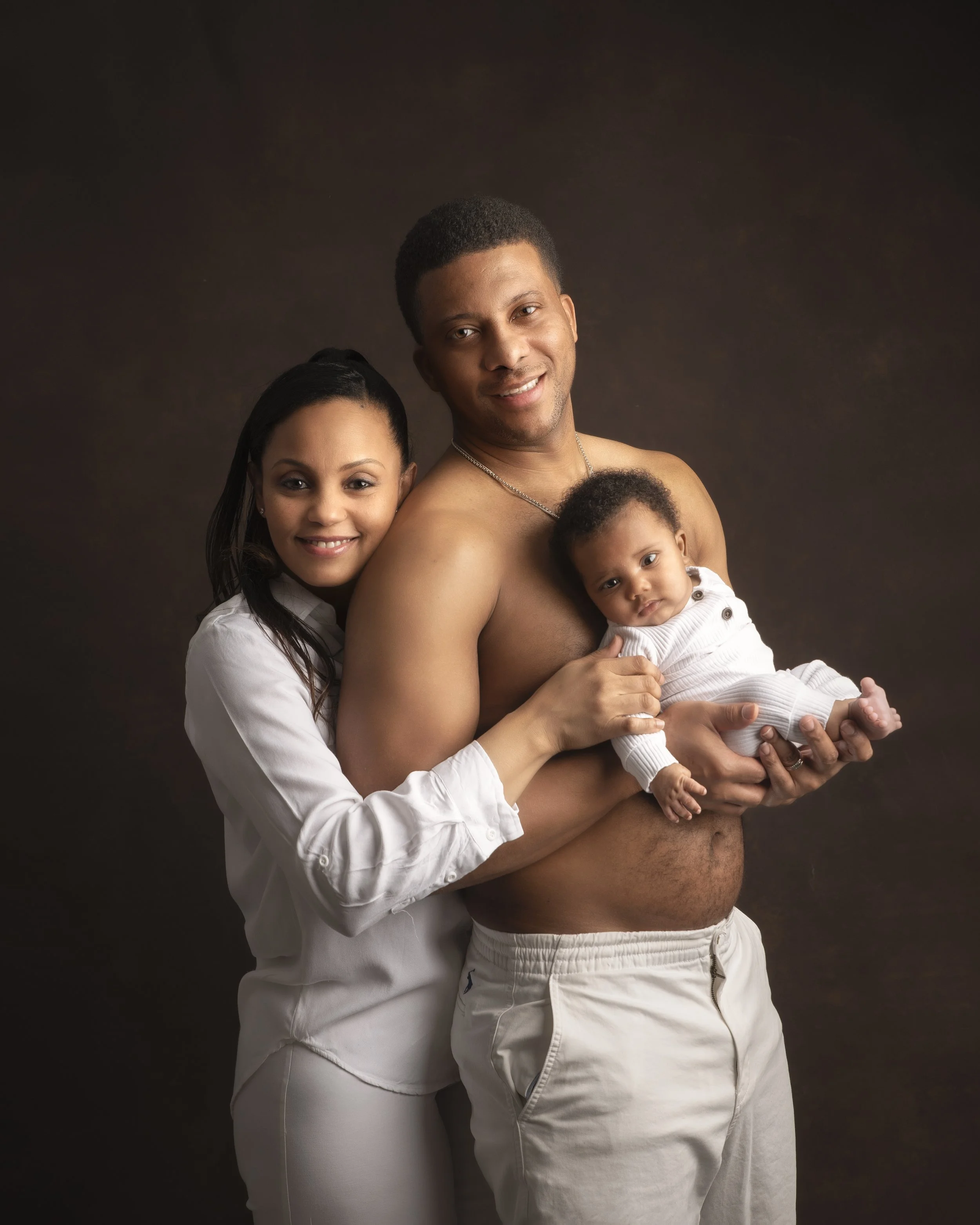 A happy family portrait with a man, a woman, and a baby against a dark background.