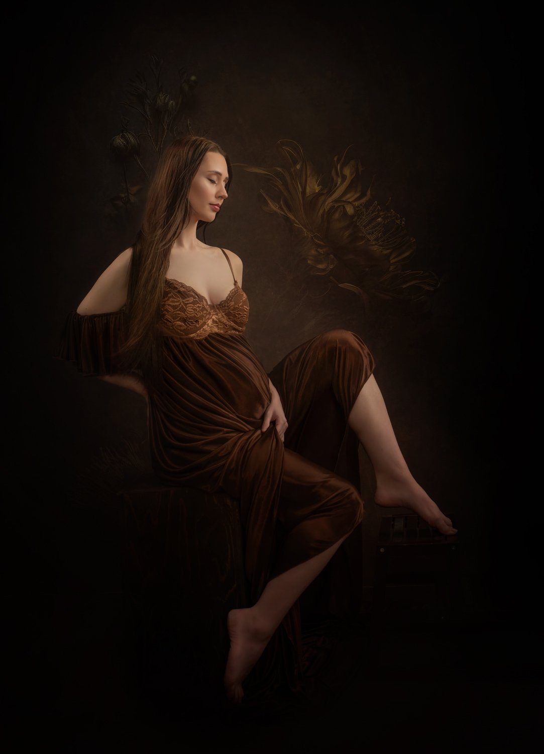 A woman with long brown hair in a brown dress sitting on a dark chair against a dark background with feather-like patterns.