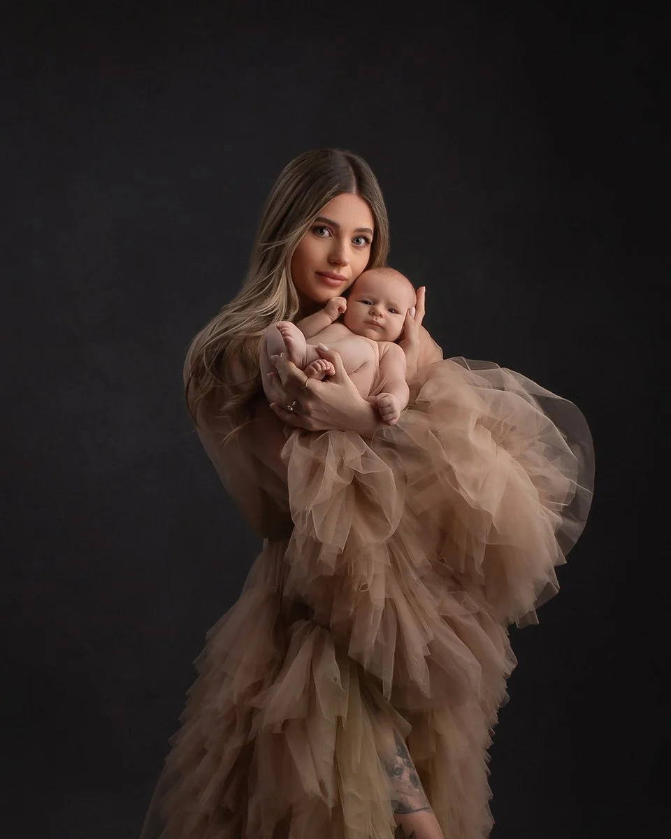 Photoshoot by Ally, Photoshoot by Ally, A woman with long hair holding a baby girl, both dressed in matching beige fluffy dresses, against a black background.