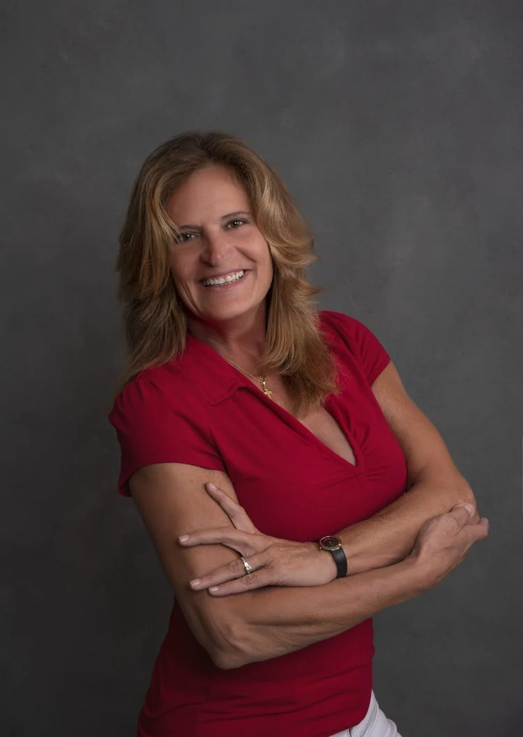 Headshots by Ally, A smiling woman with shoulder-length blonde hair wearing a red short-sleeve shirt, standing against a gray background.