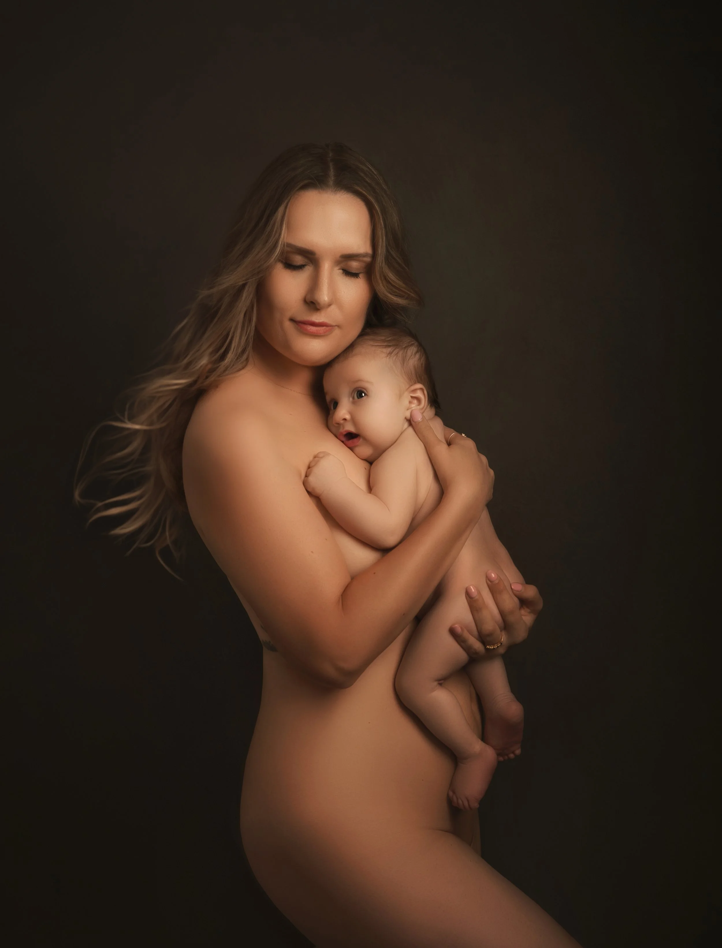 A woman holding a baby in her arms against a dark background.