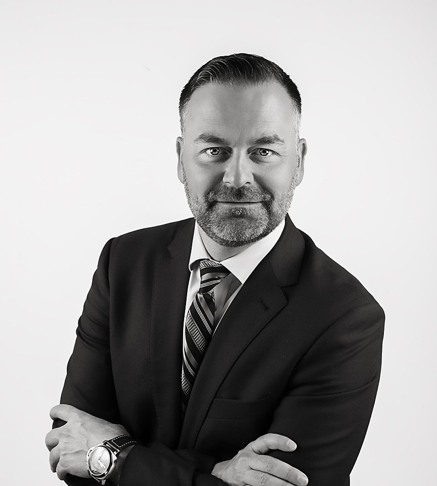 Headshots by Ally, Black and white portrait of a middle-aged man with short hair and a beard, wearing a suit and tie, crossing his arms.