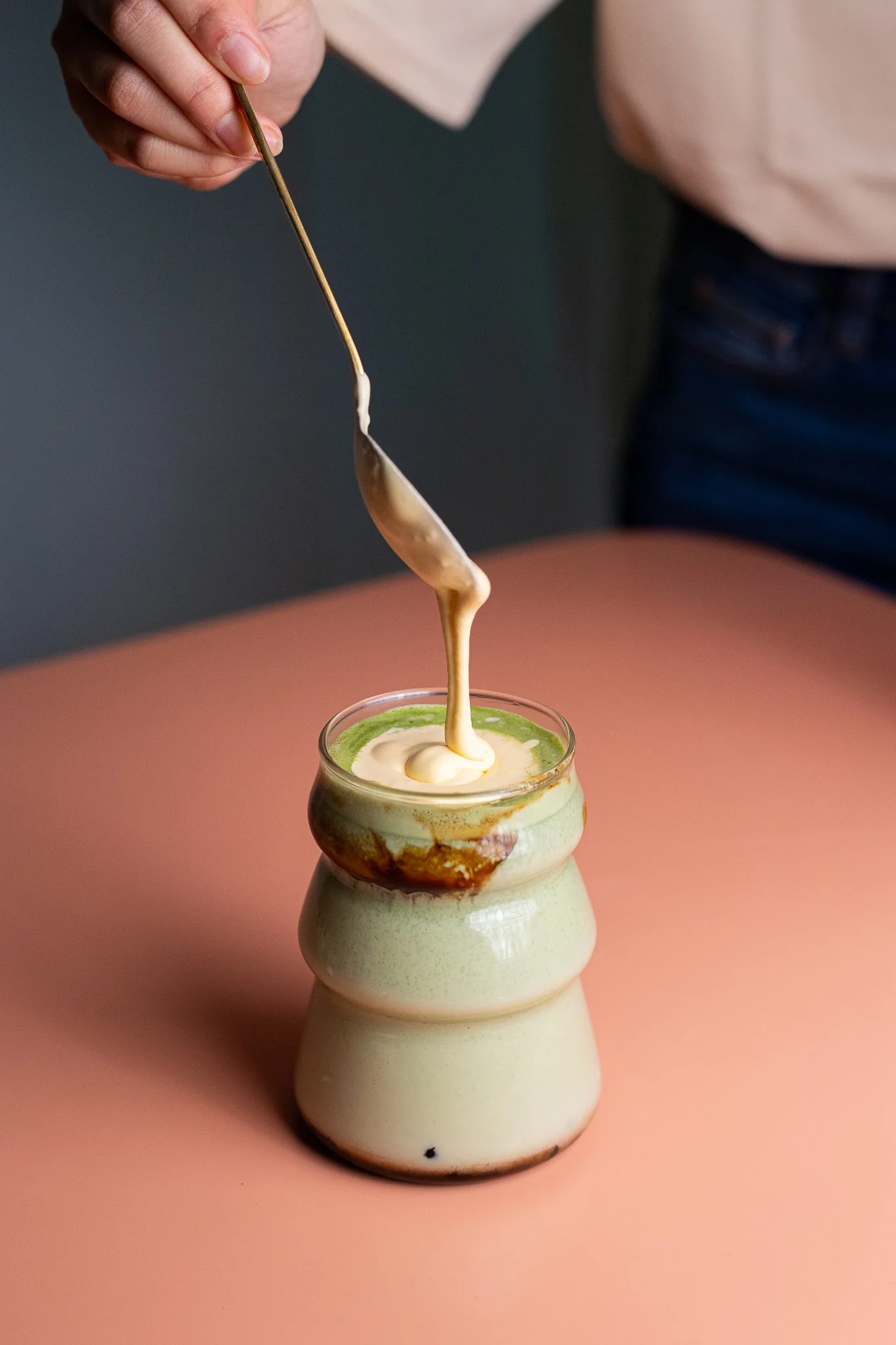 Une main verse de la crème ou du caramel dans un pot en céramique avec une surface mousseuse.