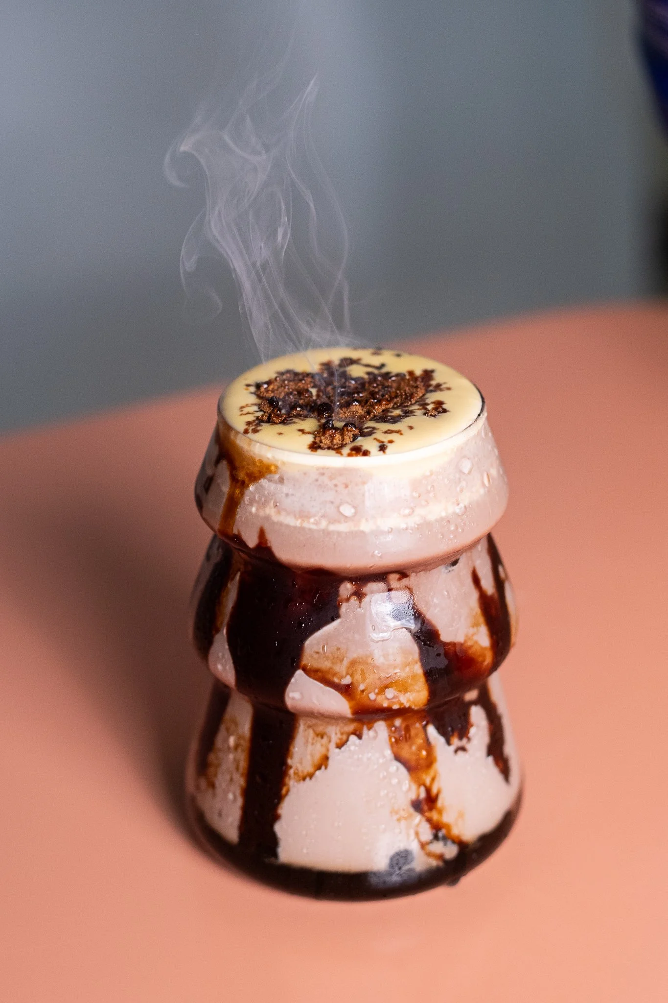 Un cocktail chaud dans un verre en forme de poupée avec de la mousse et du chocolat fondu sur le dessus, avec de la vapeur qui s'élève.