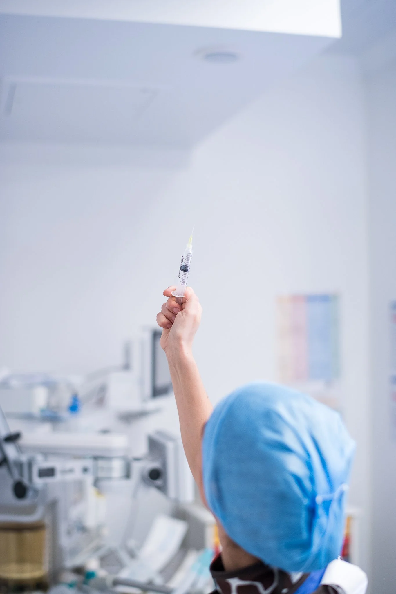 Une main d'une personne en tenue chirurgicale tenant une seringue dans un environnement médical.