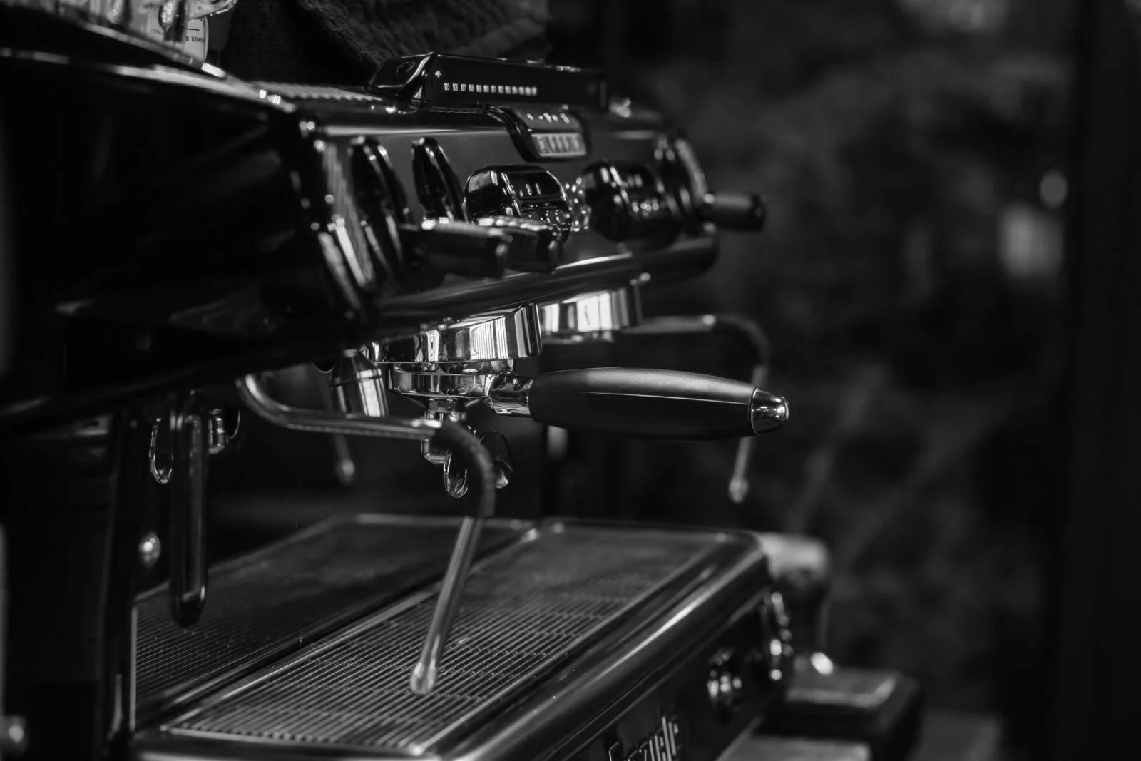 Black and white image of a vintage espresso machine with chrome details and a portafilter handle.
