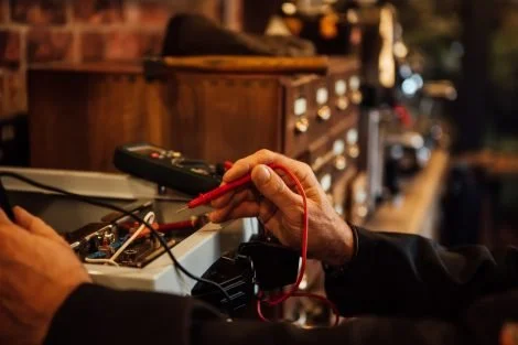 Close-up of a person testing electrical components with a multimeter and red banana probe on an electronic device.
