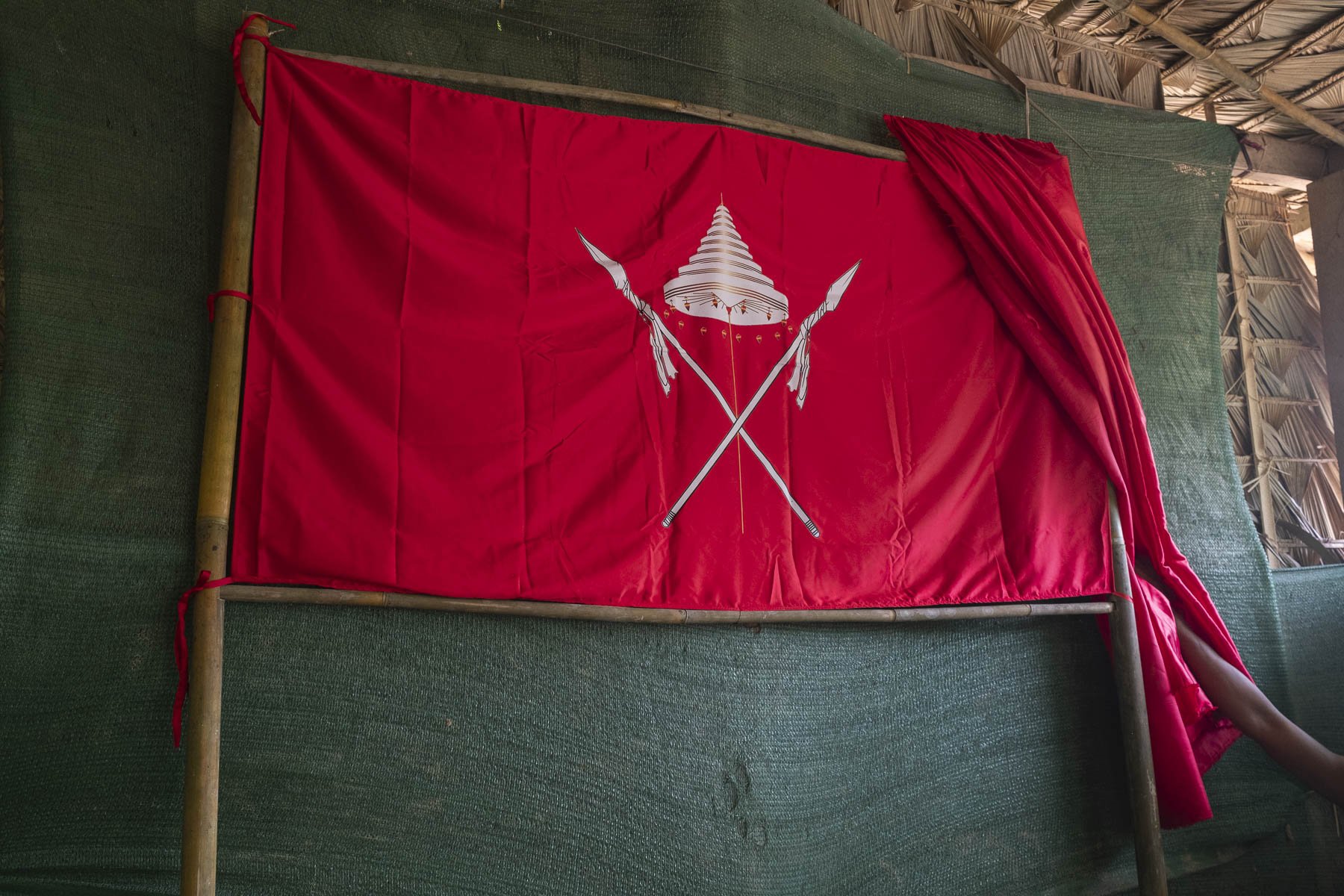 Red flag with a white emblem of a pagoda and two crossed spears, attached to a bamboo frame, partially unfurled.