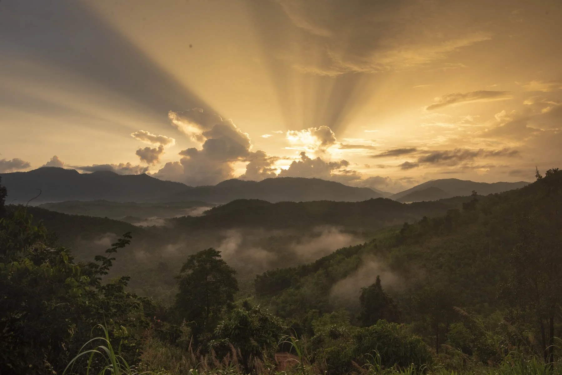 Sunrise over a misty mountain landscape with clouds and rays of sunlight shining through.