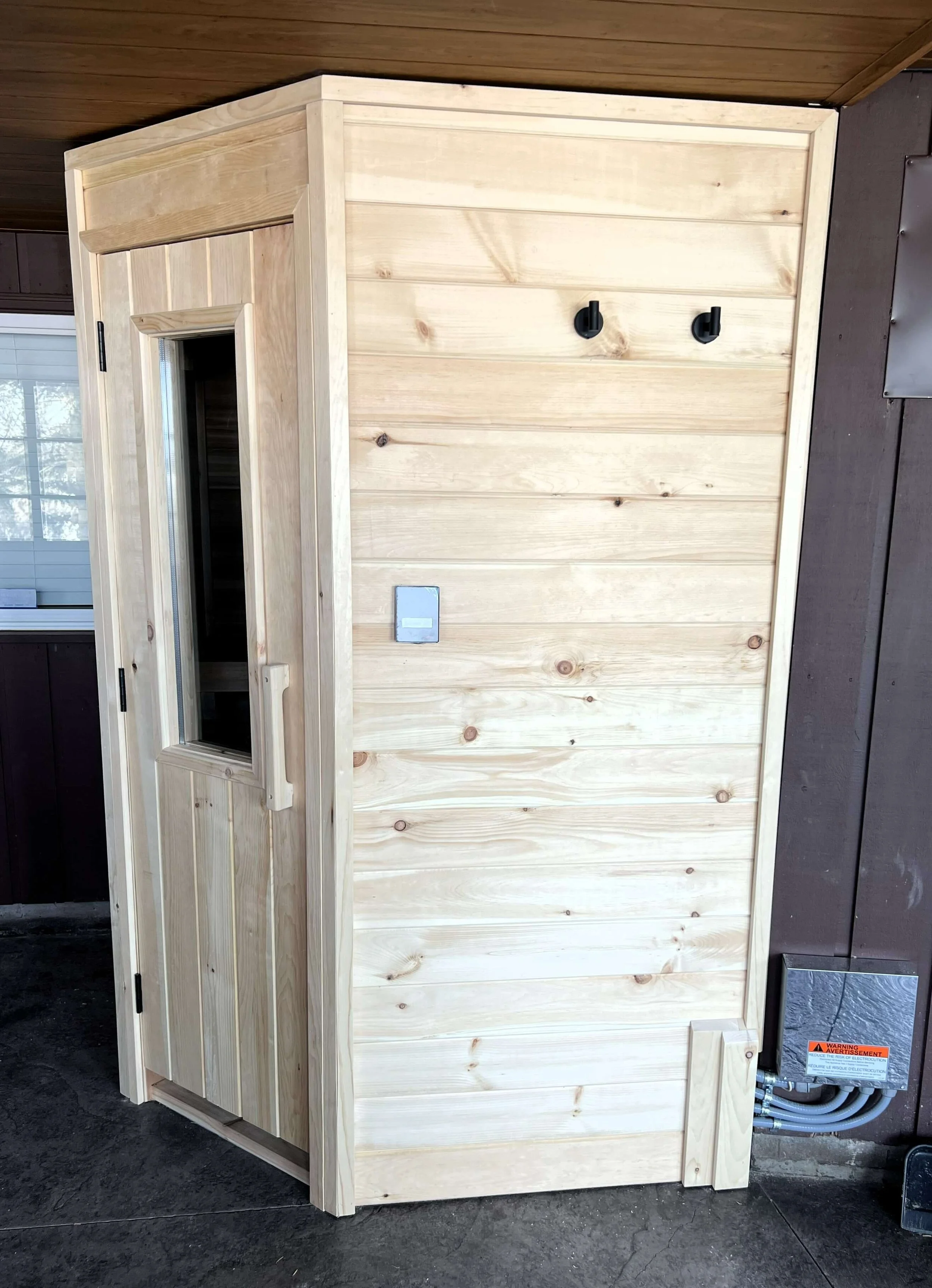 Custom 2-person outdoor sauna built in Kawartha Lakes, Ontario with pine exterior and thermopane window.