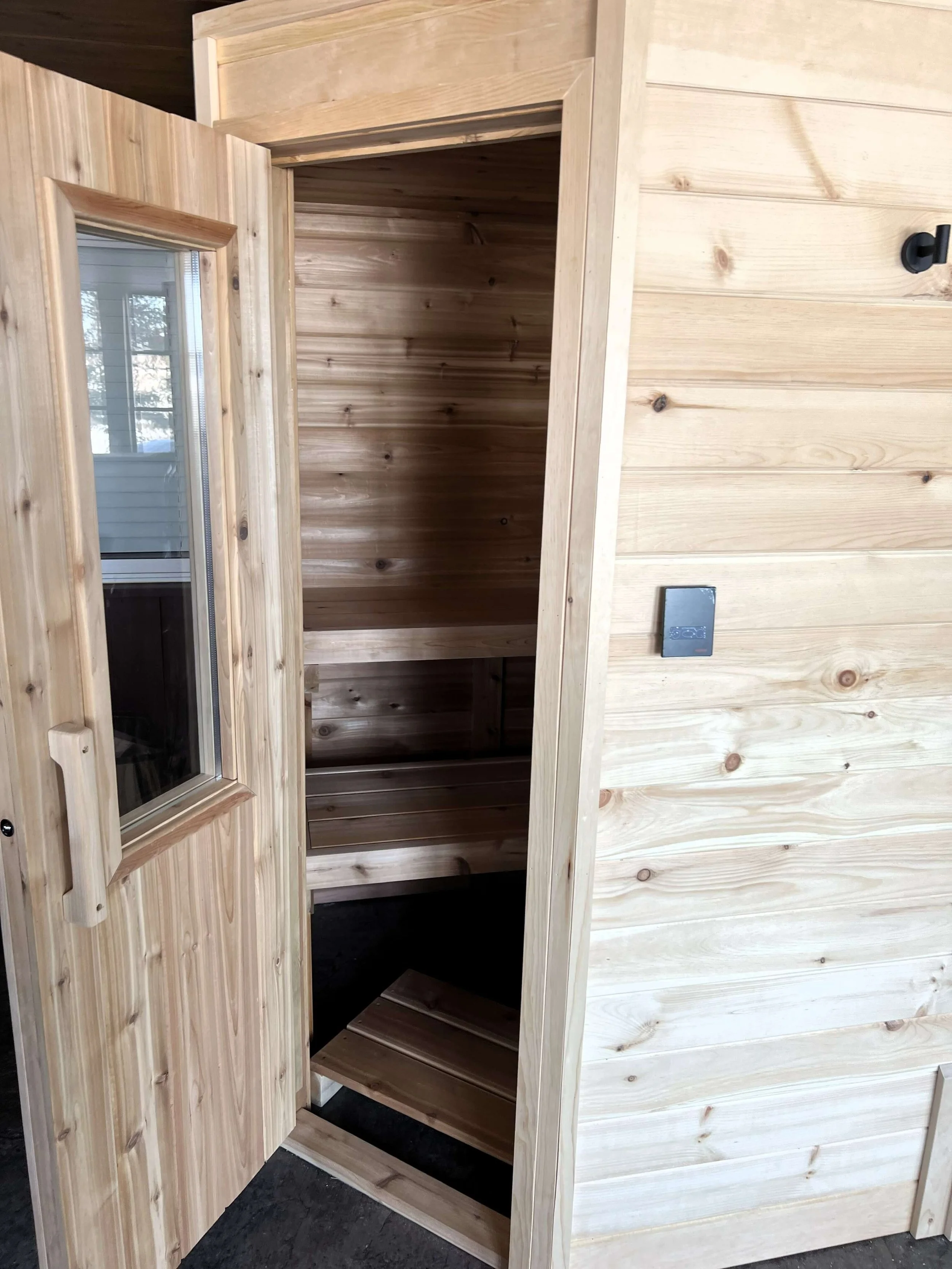Open door view of custom Western Red Cedar sauna interior showing upper and sliding lower bench with natural lighting.